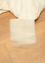 White fabric on a wooden surface with a clear square piece of paper.
