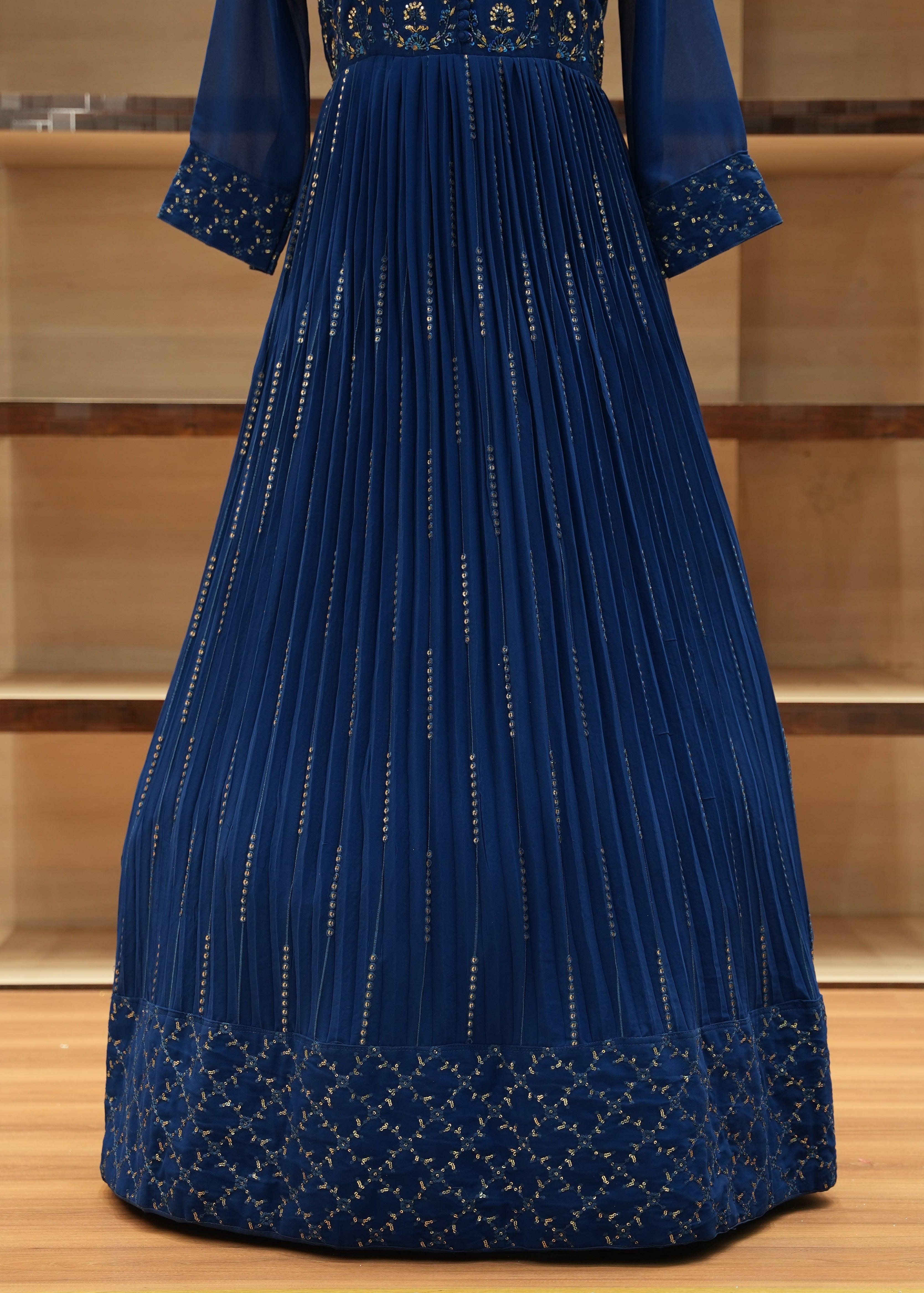 Blue pleated dress with gold detailing on a wooden surface