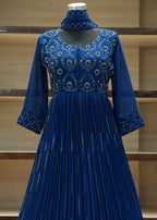 Blue dress with intricate patterns on a mannequin against a wooden shelf background