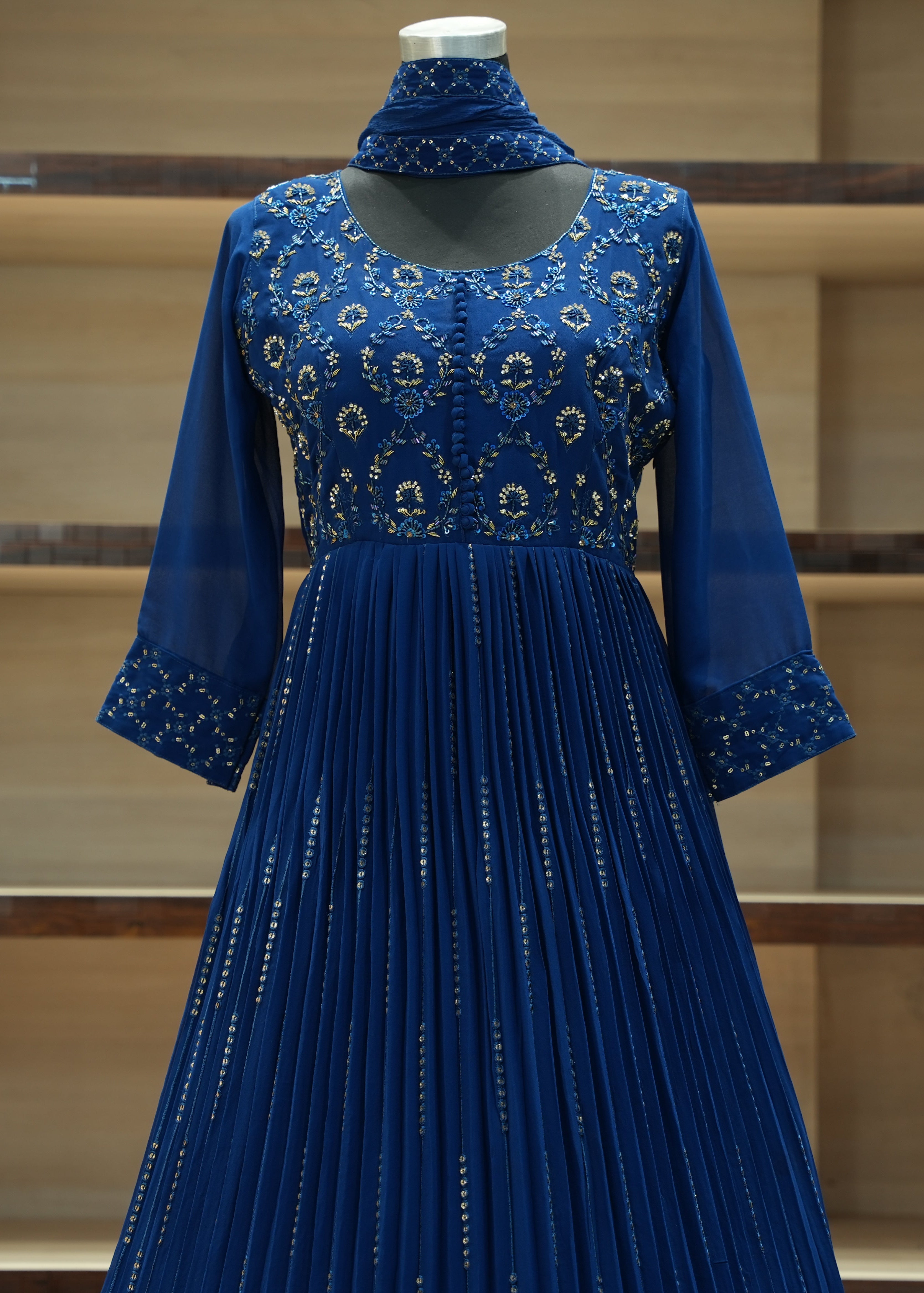 Blue dress with intricate patterns on a mannequin against a wooden shelf background