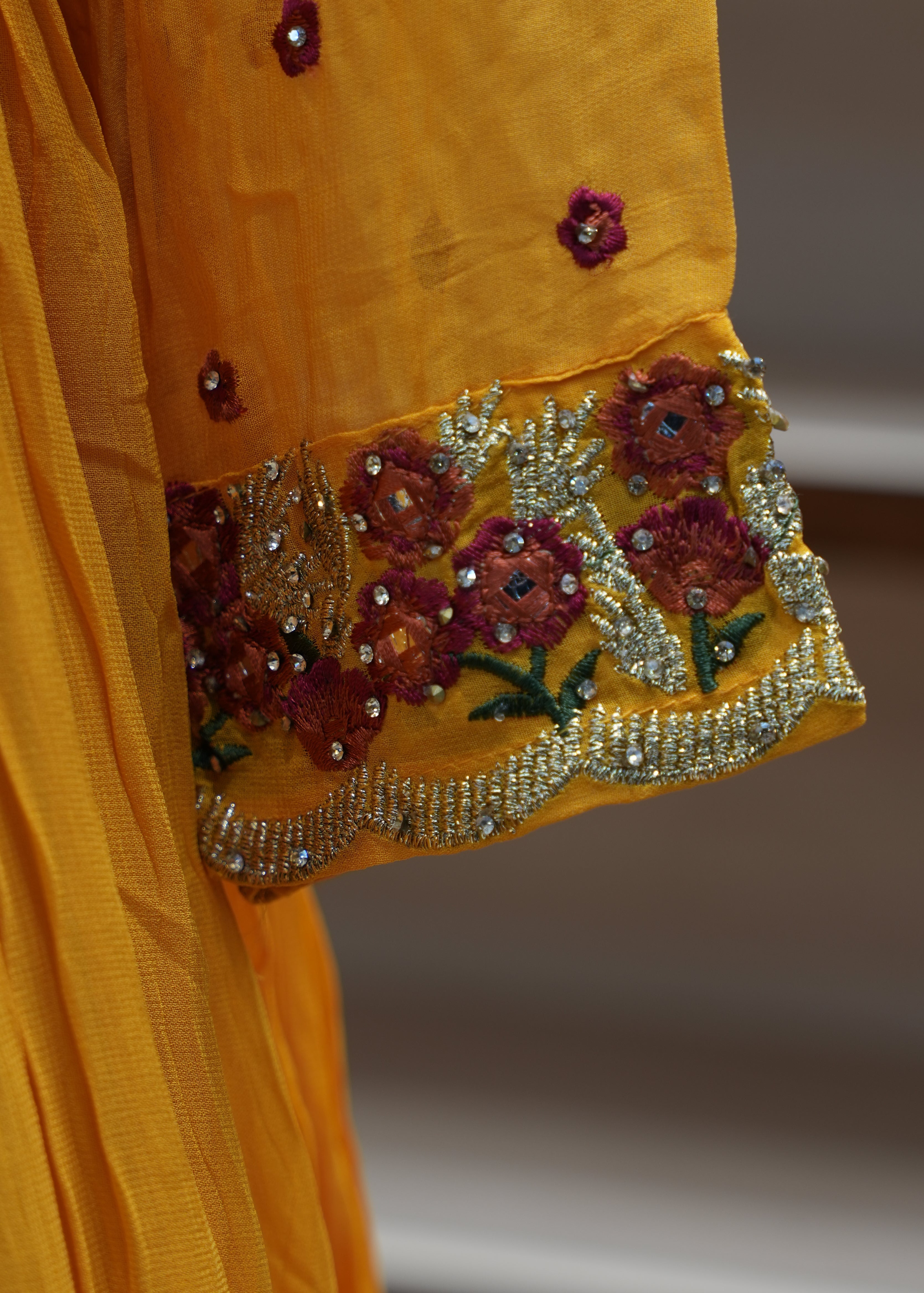 Close-up of a yellow fabric with floral embroidery and beadwork on a plain background