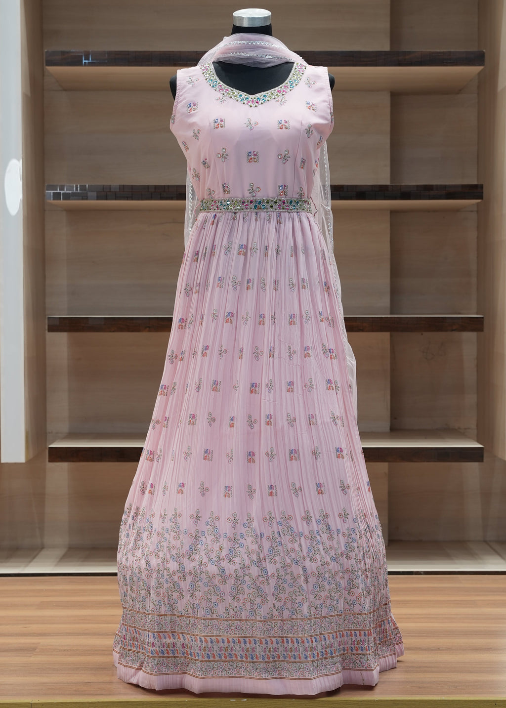 Pink embroidered dress on a mannequin against a wooden panel background