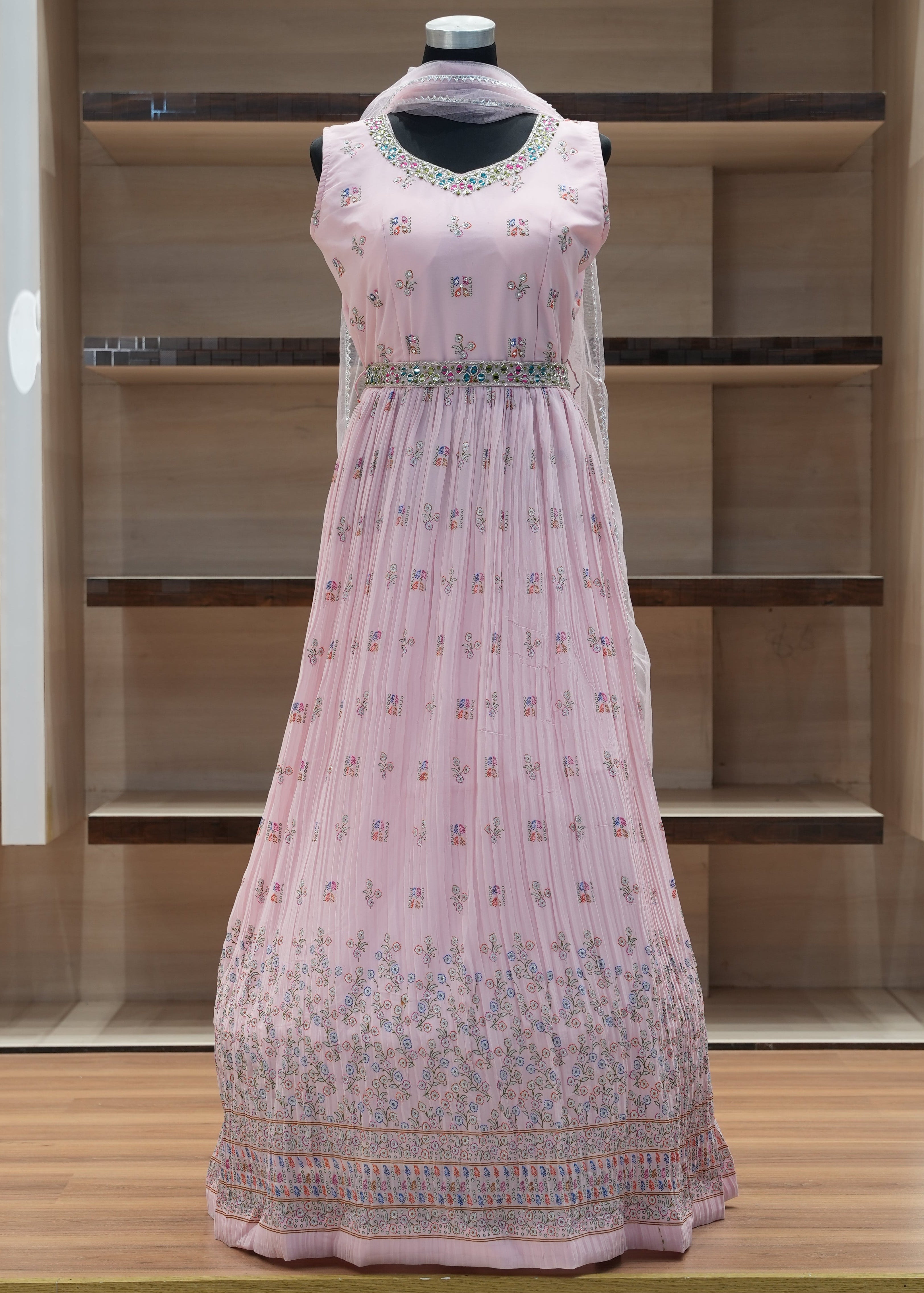 Pink embroidered dress on a mannequin against a wooden panel background