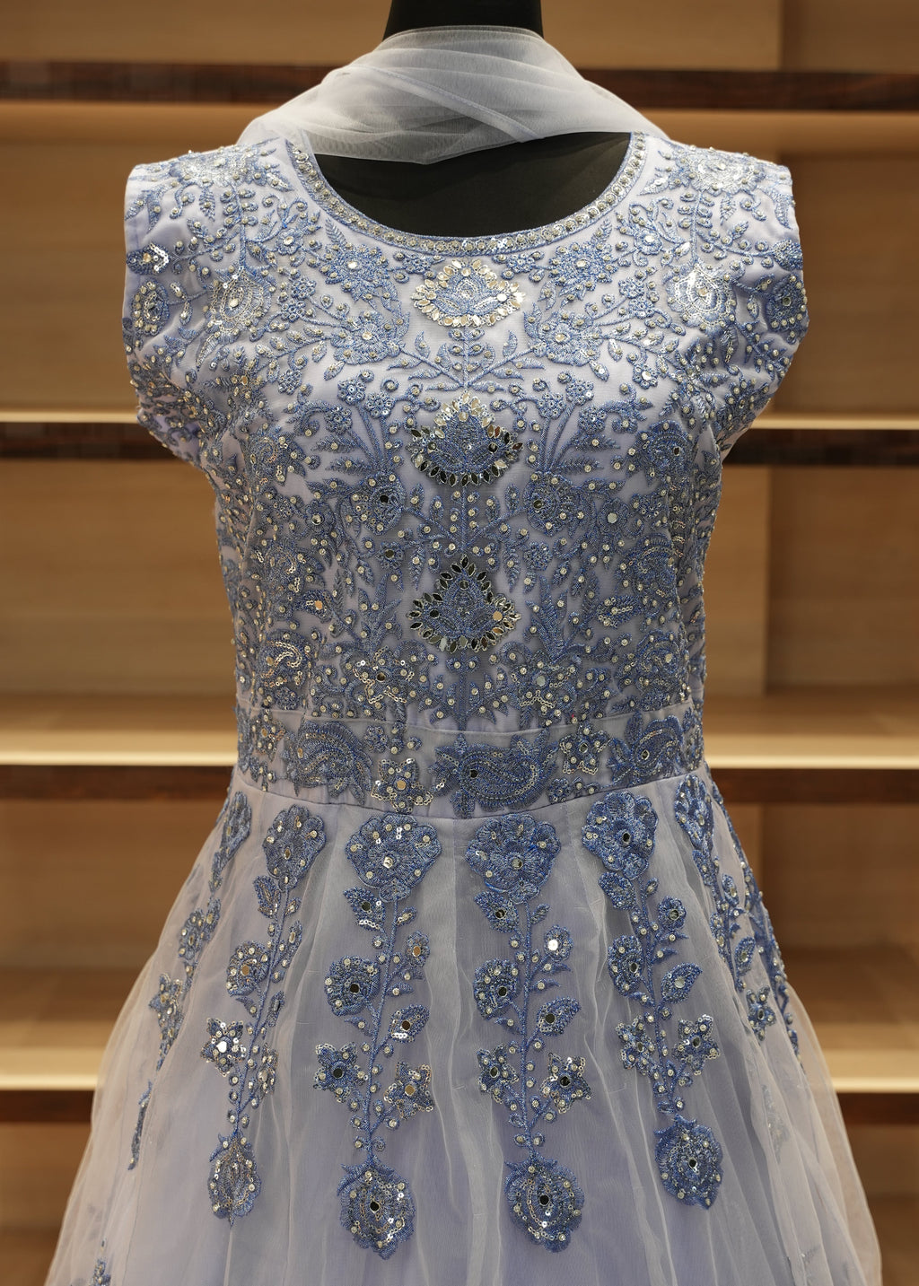 Blue evening gown with intricate beadwork on a wooden stand.
