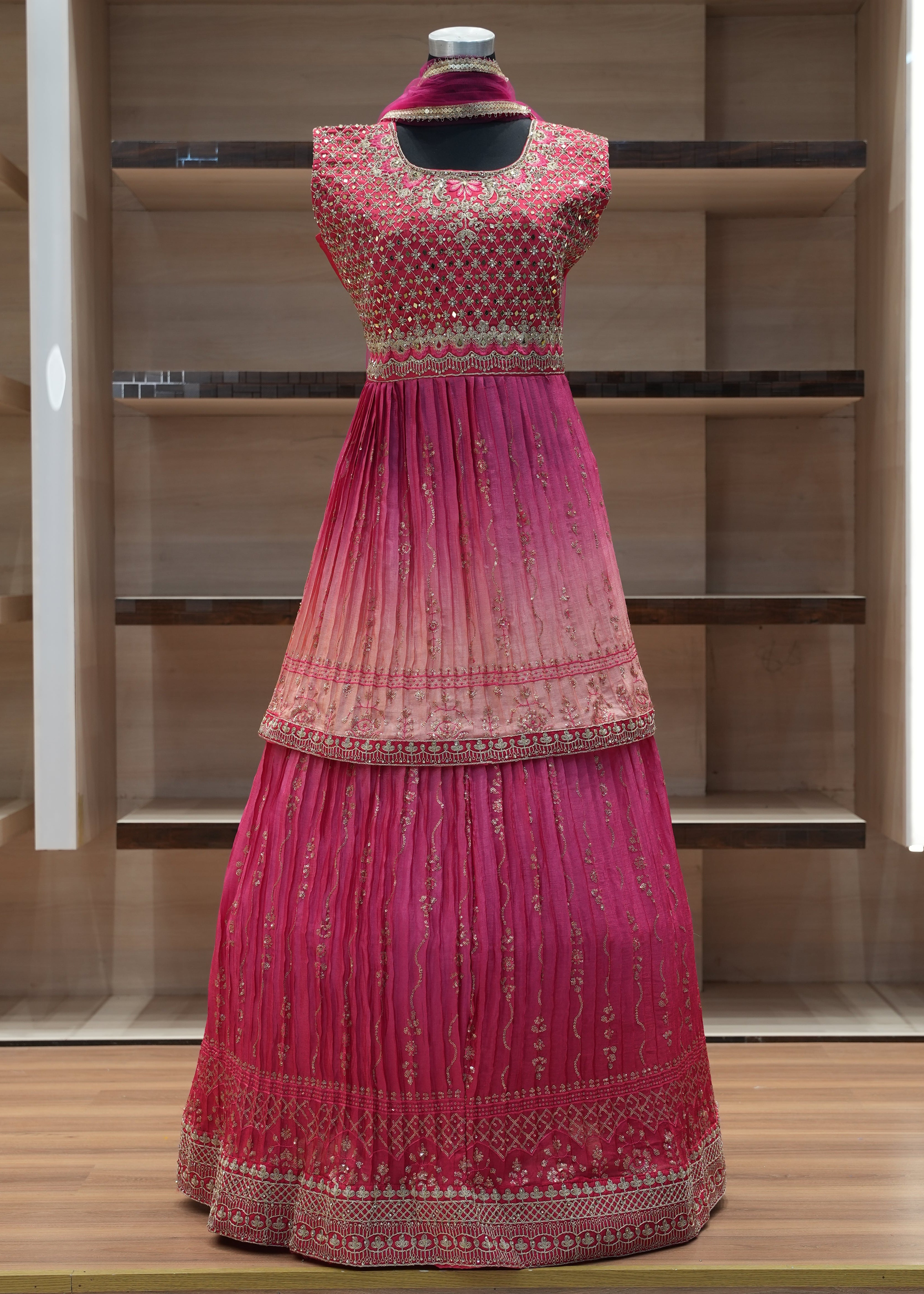 Mannequin wearing a pink traditional outfit with intricate designs against a wooden background