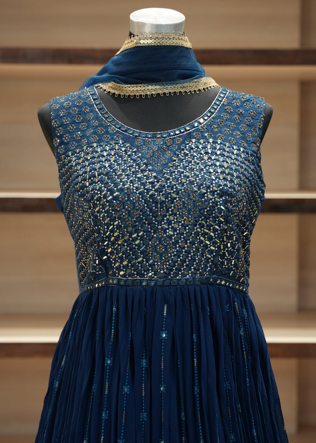 Blue dress with intricate detailing on a wooden mannequin against a wooden panel background
