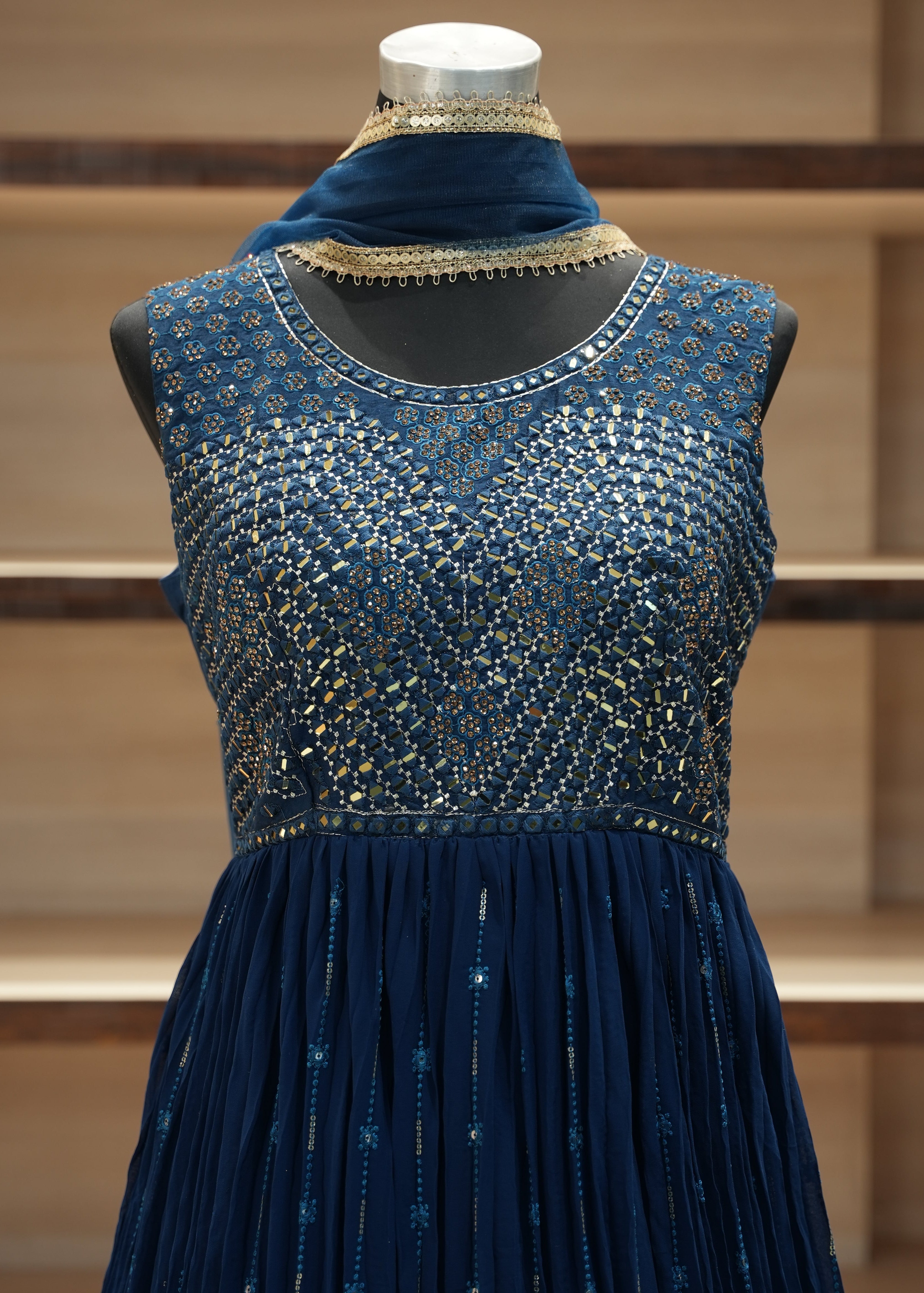 Blue dress with intricate detailing on a wooden mannequin against a wooden panel background