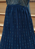 Close-up of a blue pleated dress with a textured fabric against a beige curtain background