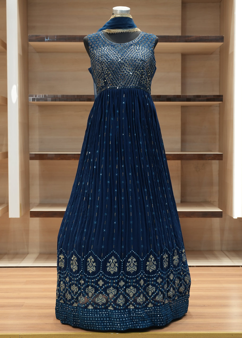 Blue dress with intricate patterns on a wooden mannequin against a wooden background