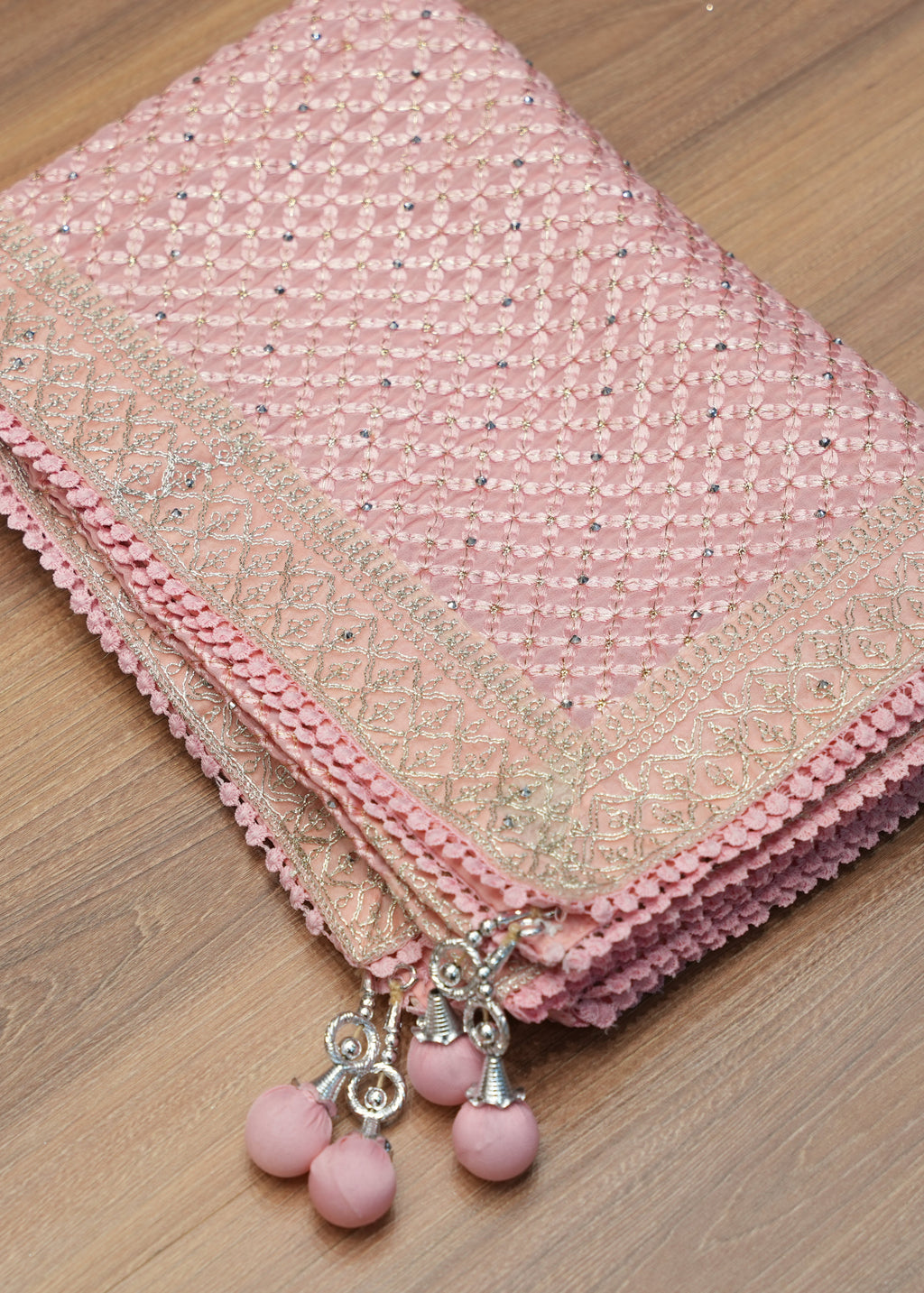 Pink fabric with decorative trim and beads on a wooden surface