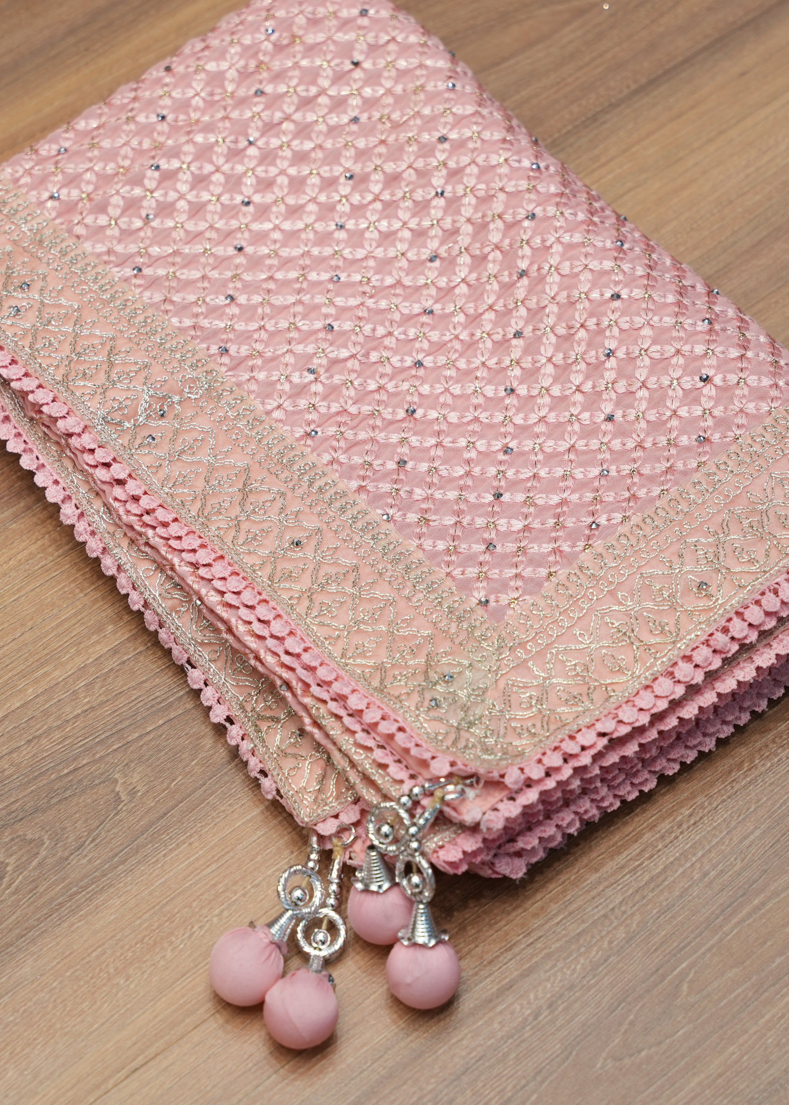 Pink fabric with decorative trim and beads on a wooden surface