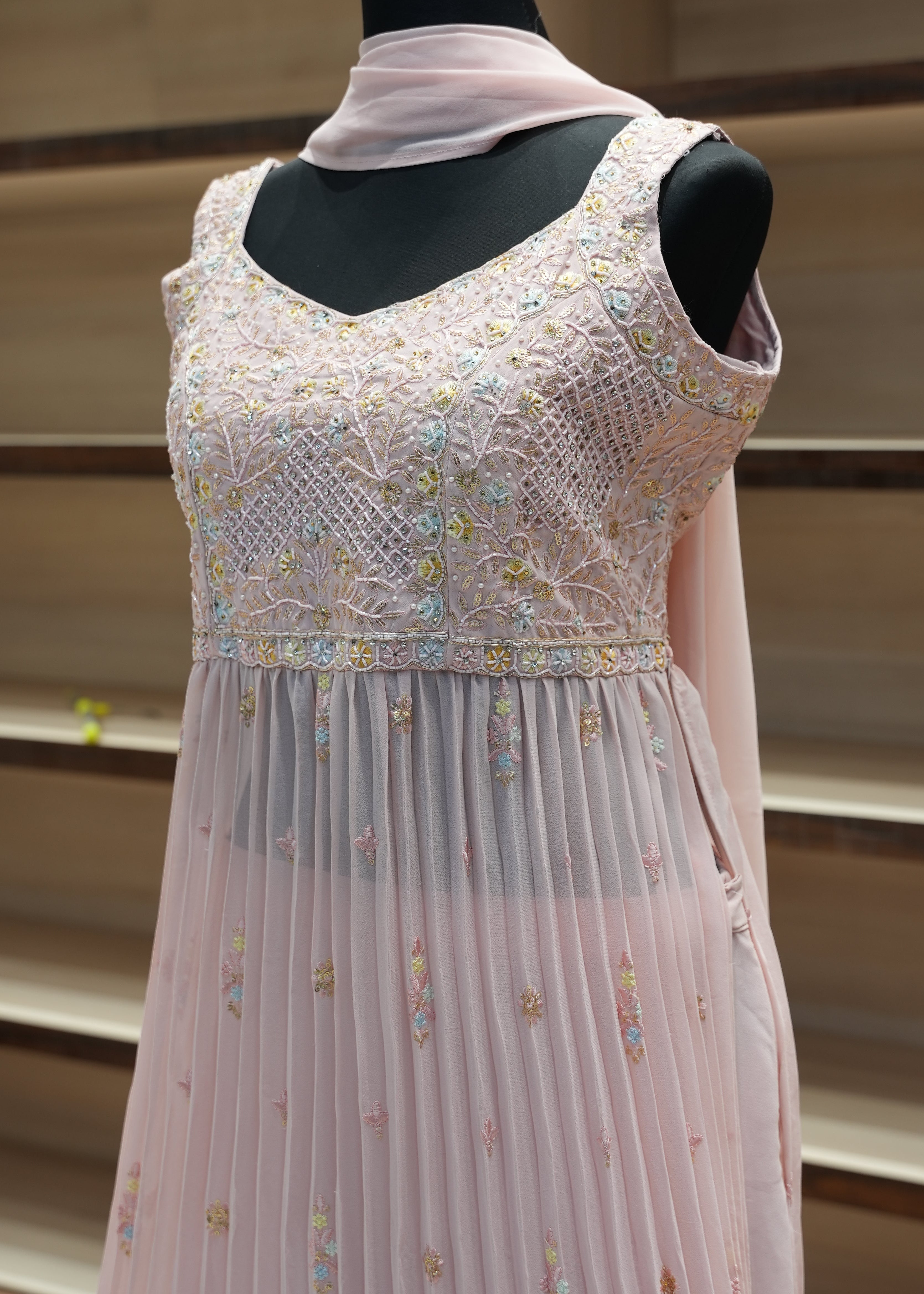 Pink dress with floral embroidery on a hanger against a neutral background