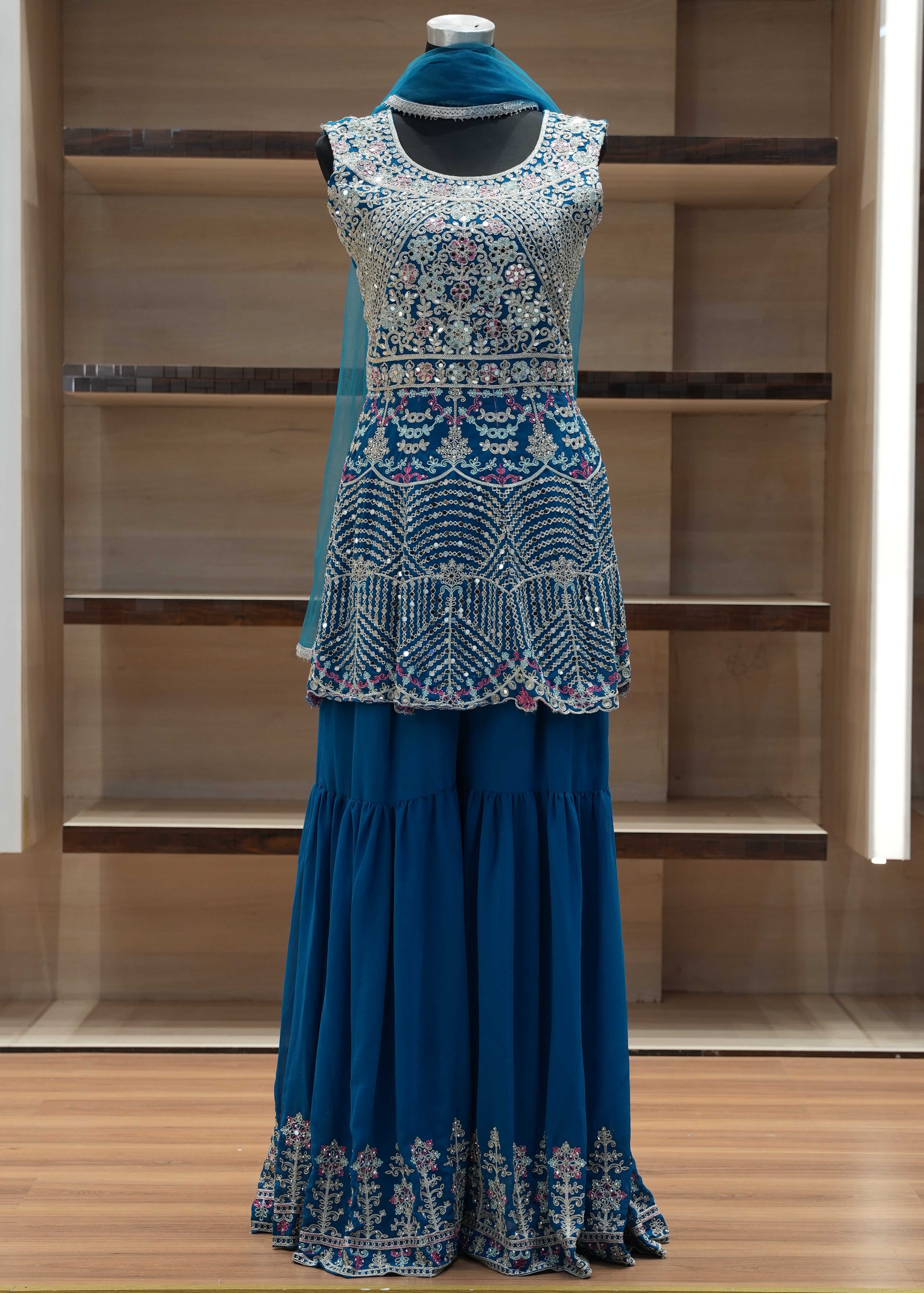 Blue dress with intricate lace detailing on a mannequin against a wooden background
