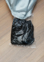 Black trash bag tied with a rubber band on a wooden floor