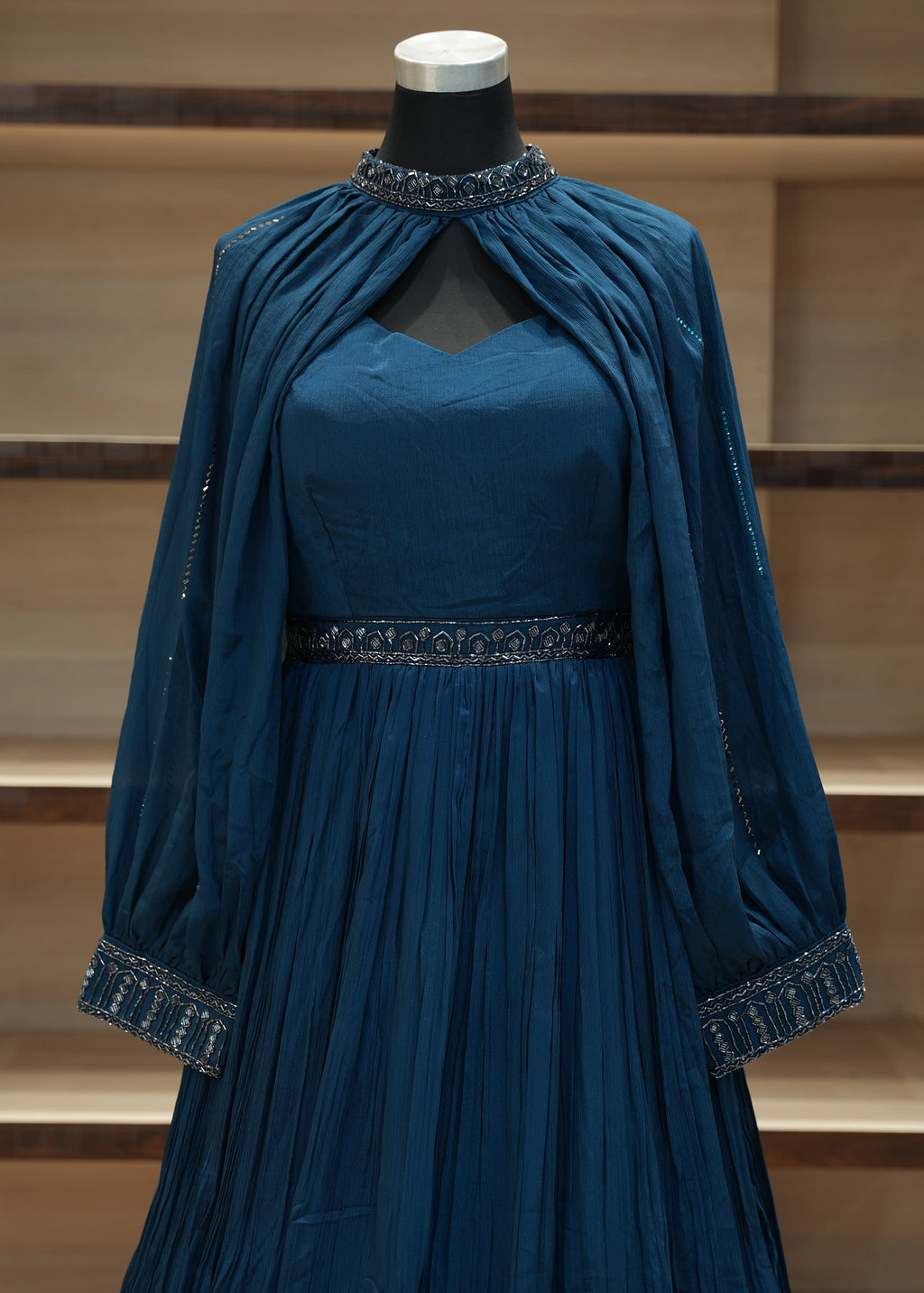Blue dress with embellishments on a wooden mannequin against a neutral background
