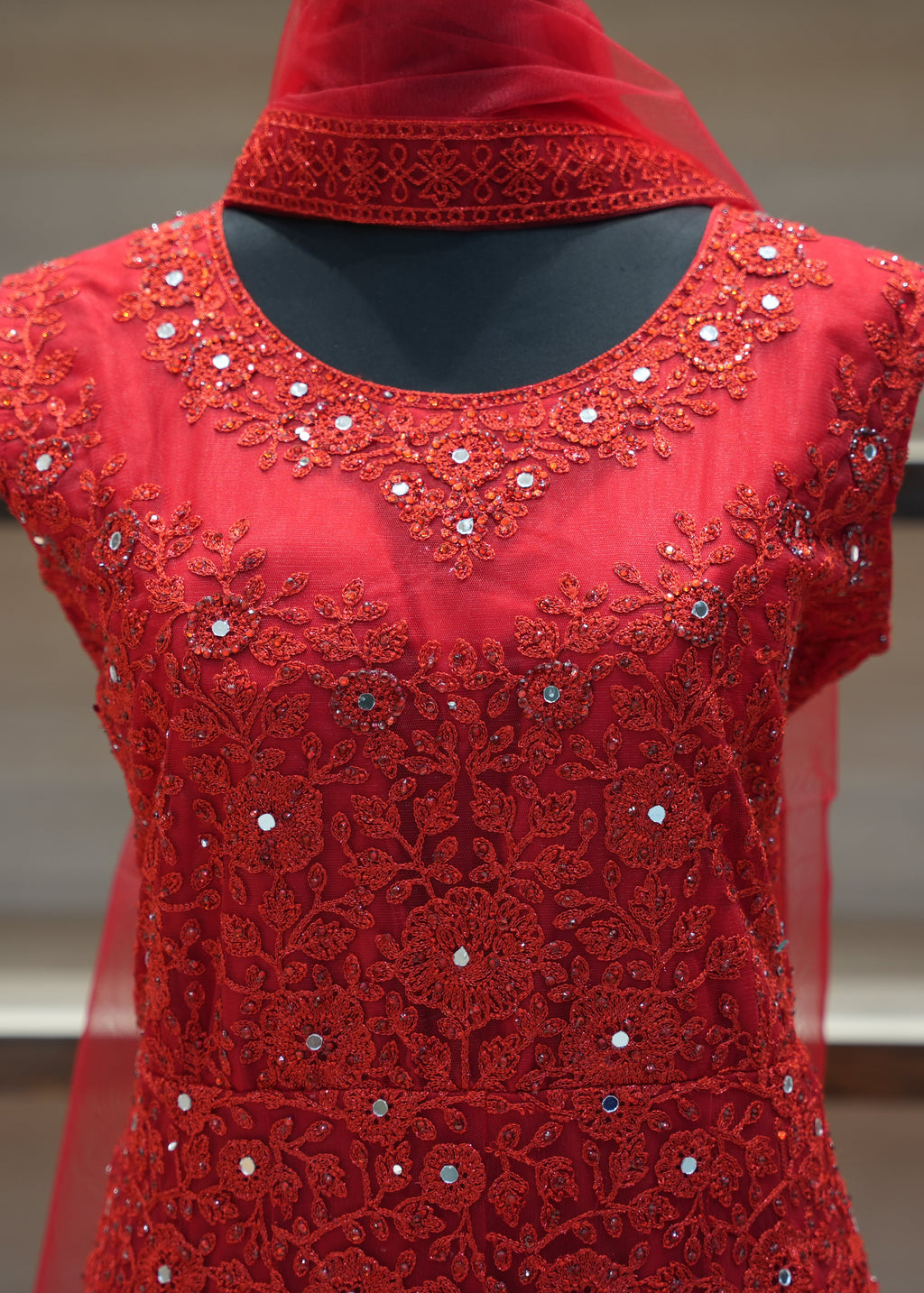 Red embroidered garment on a mannequin with a blurred background