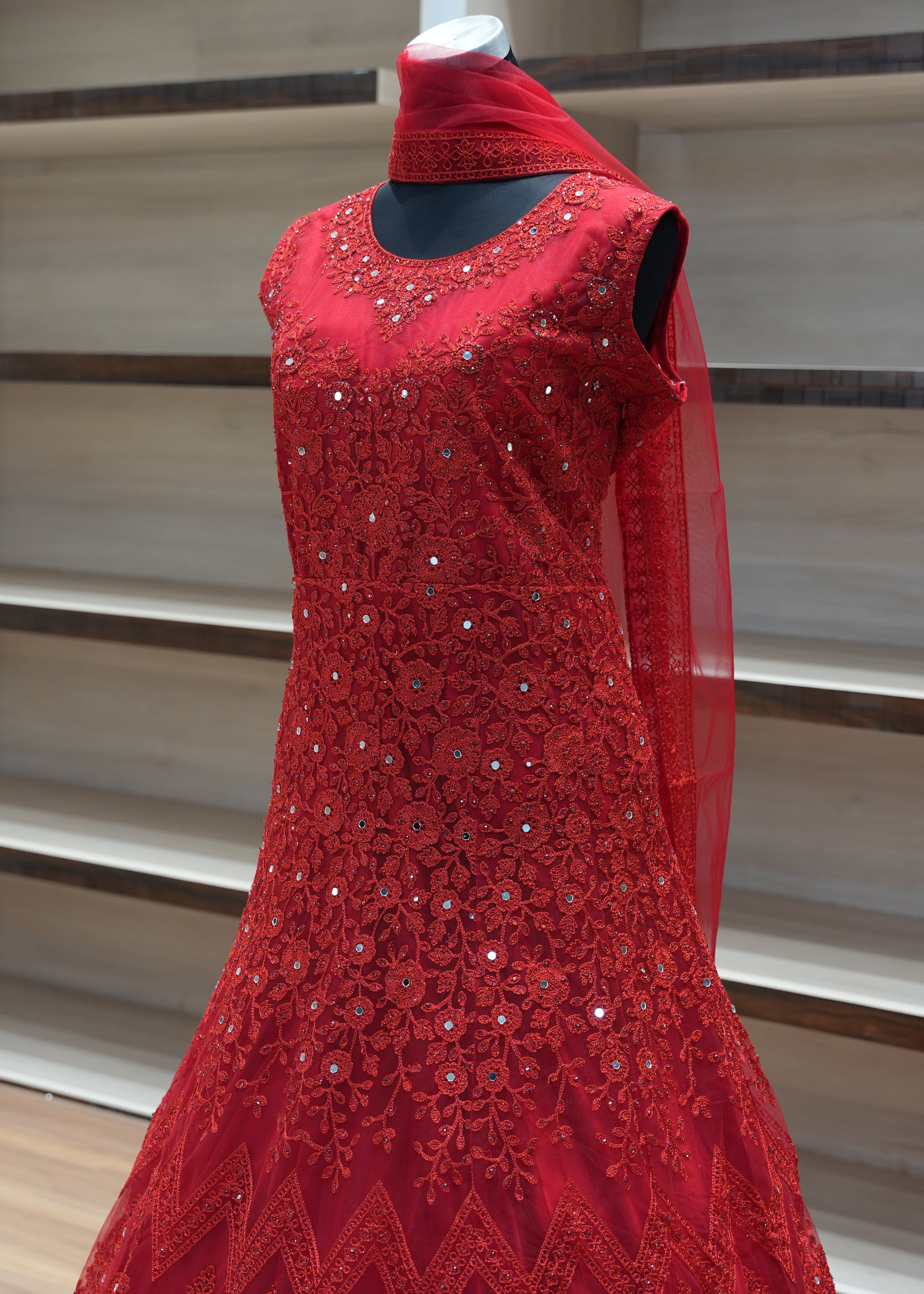 Red evening gown with intricate beading on a wooden stand.