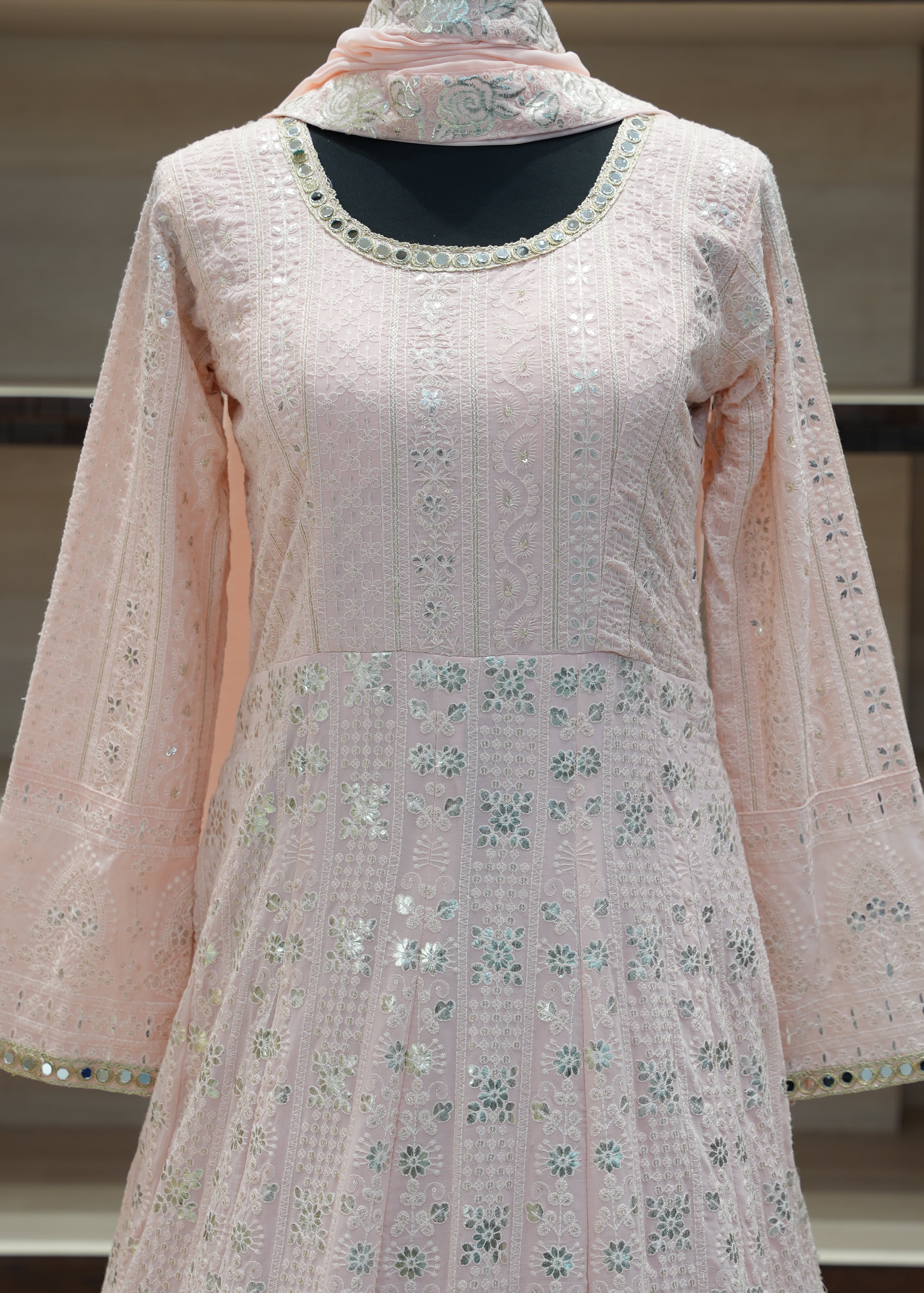 Light pink traditional outfit with floral patterns on a stand against a neutral background