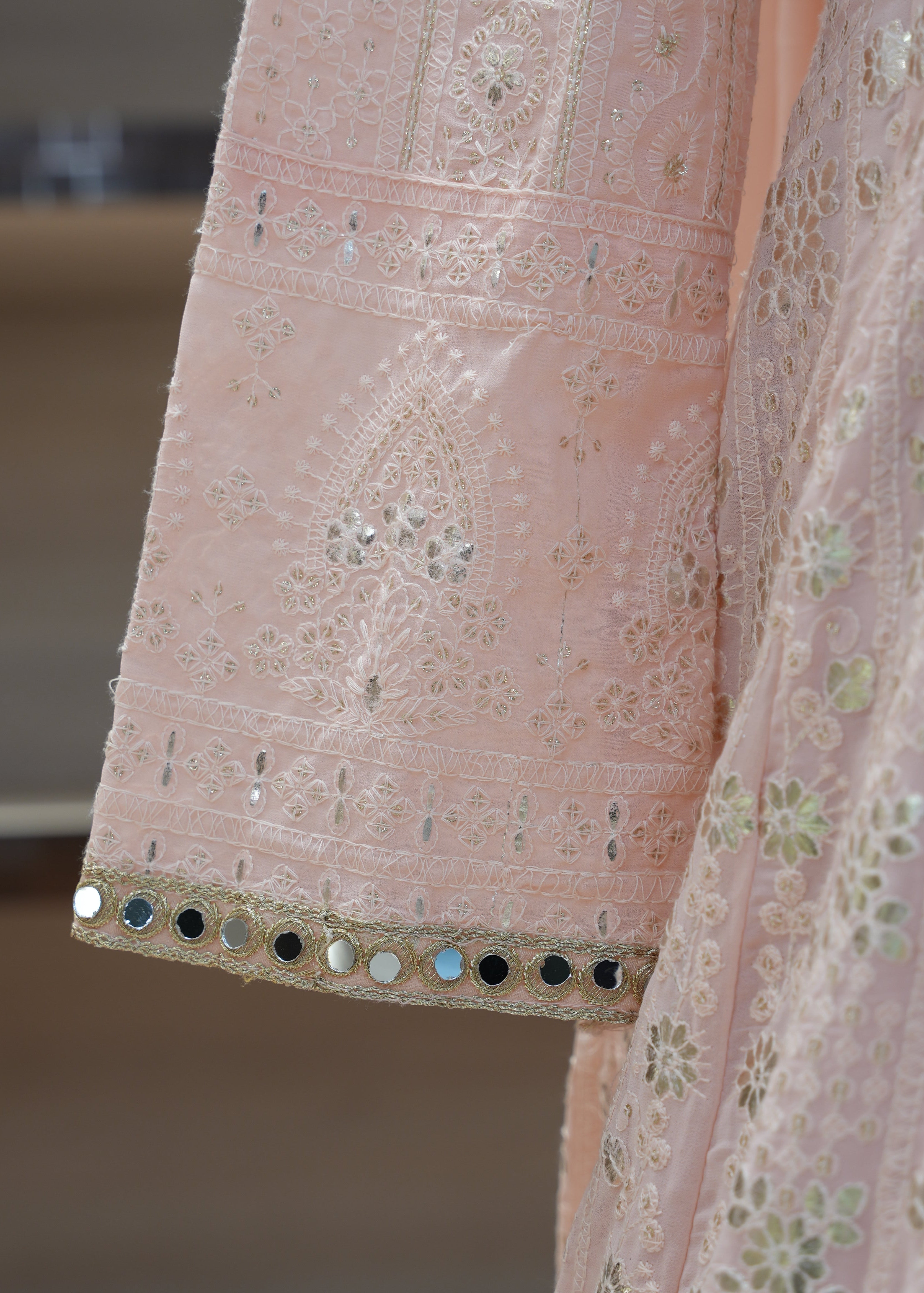 Close-up of a pink embroidered fabric with intricate patterns and mirror work.