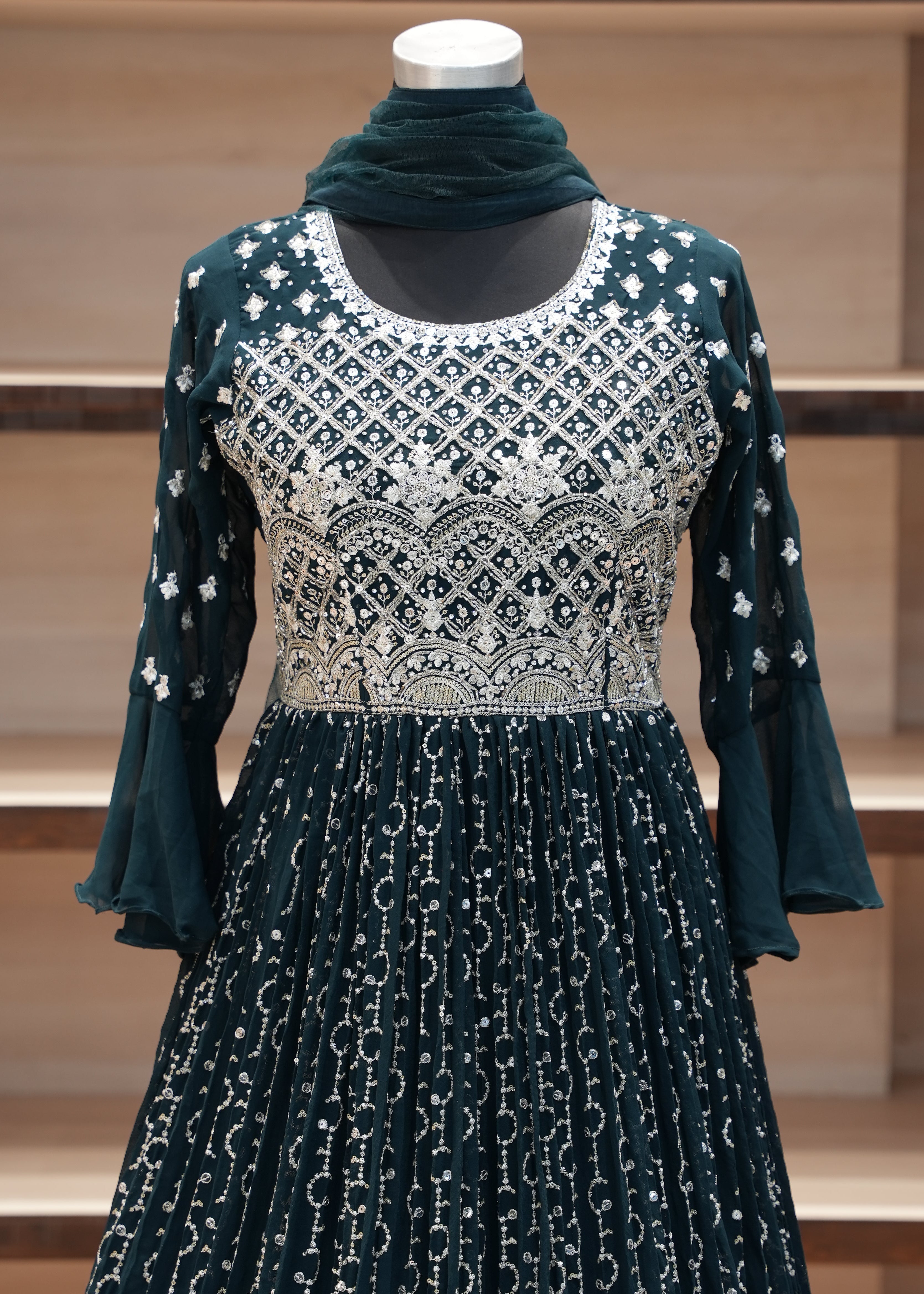 Green dress with white patterns on a mannequin against a wooden panel background