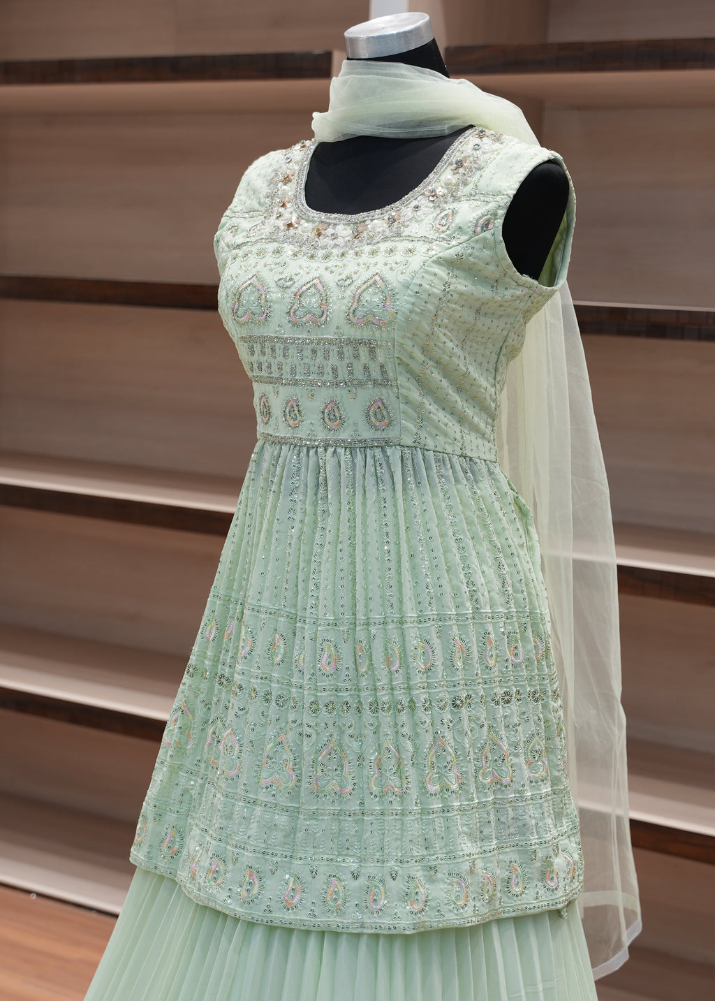 Green embroidered dress on a mannequin against a wooden panel background