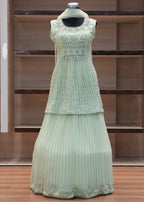 Light green pleated dress on a mannequin against a wooden panel background