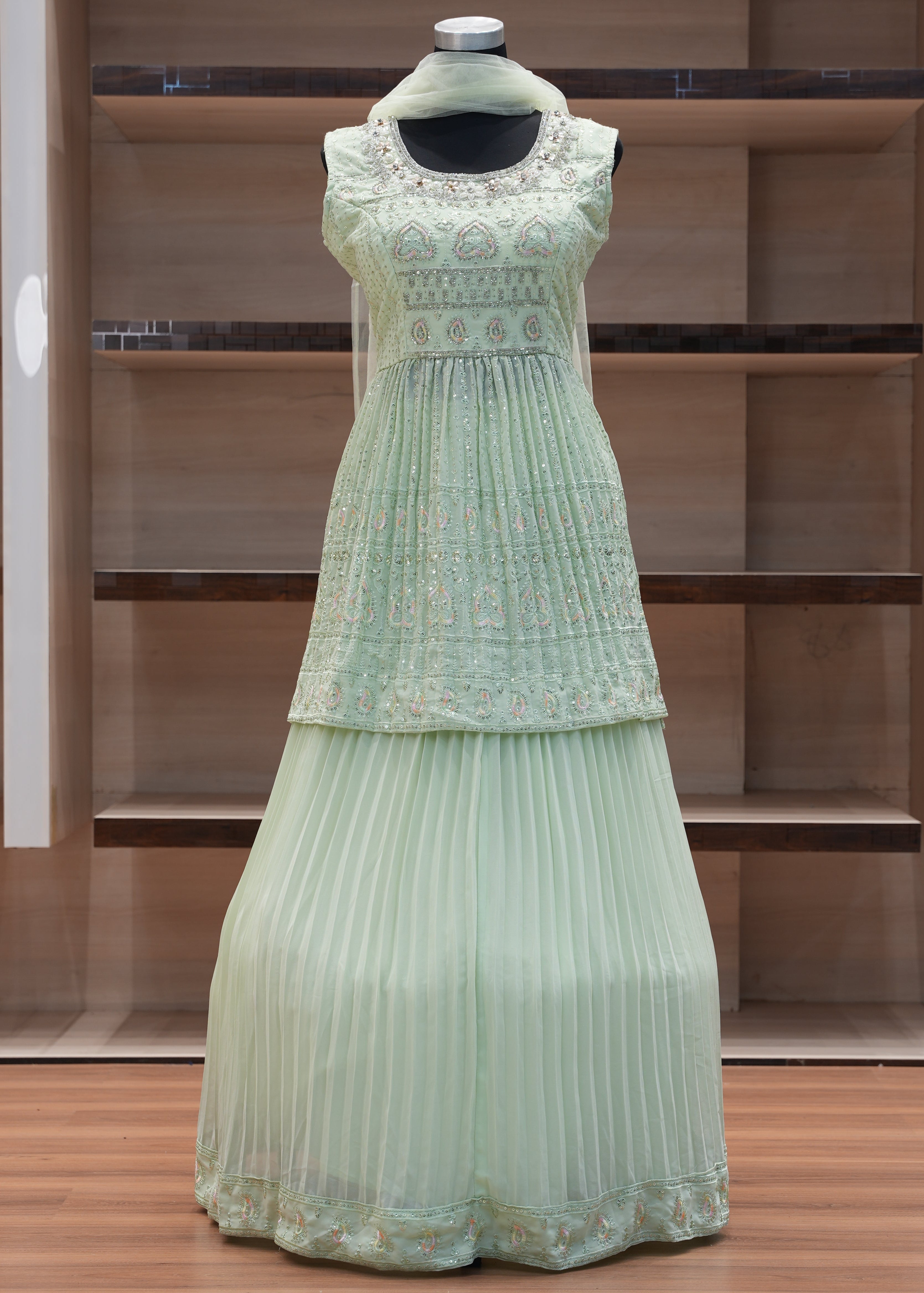 Light green pleated dress on a mannequin against a wooden panel background