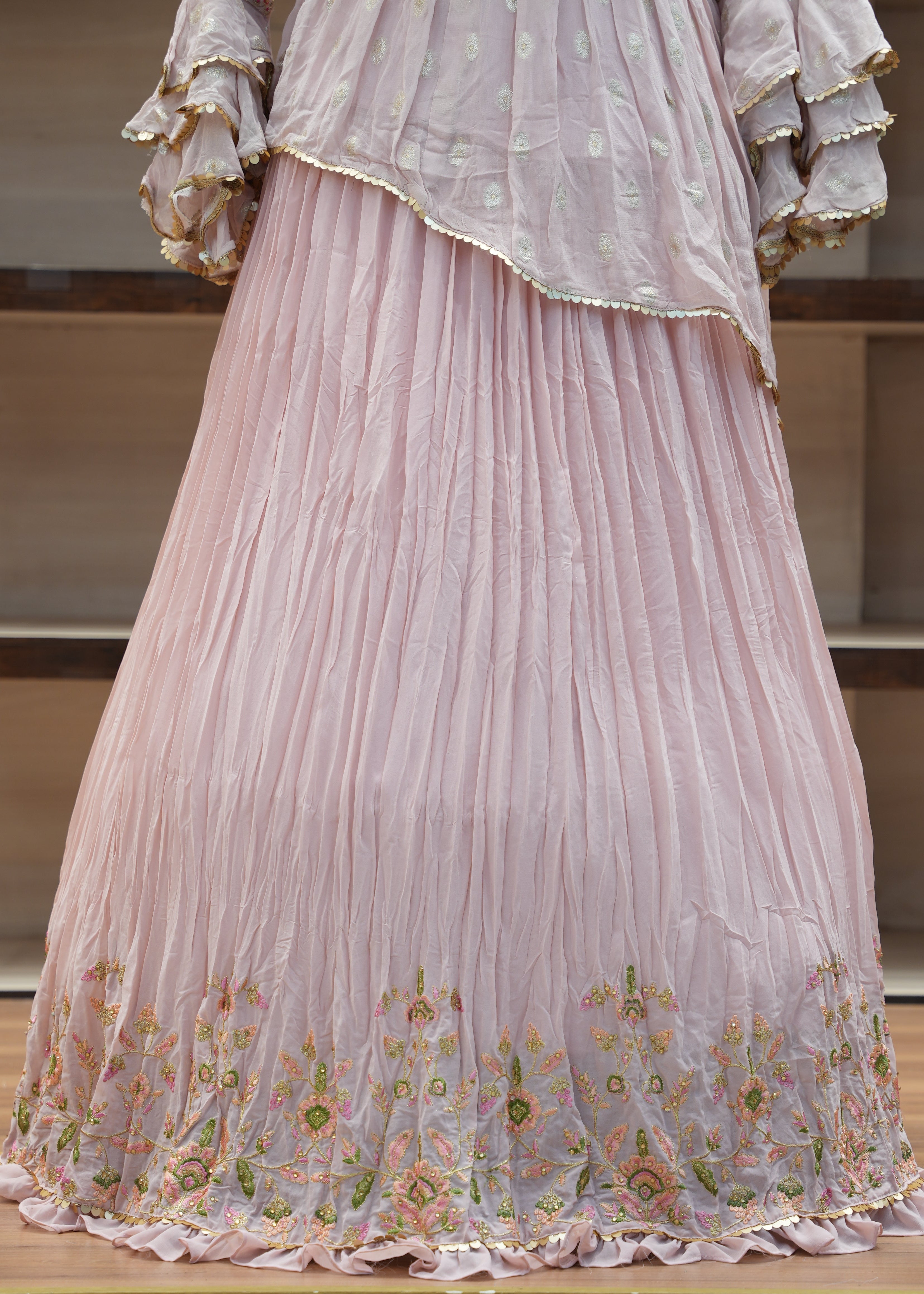 Close-up of a pink pleated fabric with floral embroidery on a wooden surface.