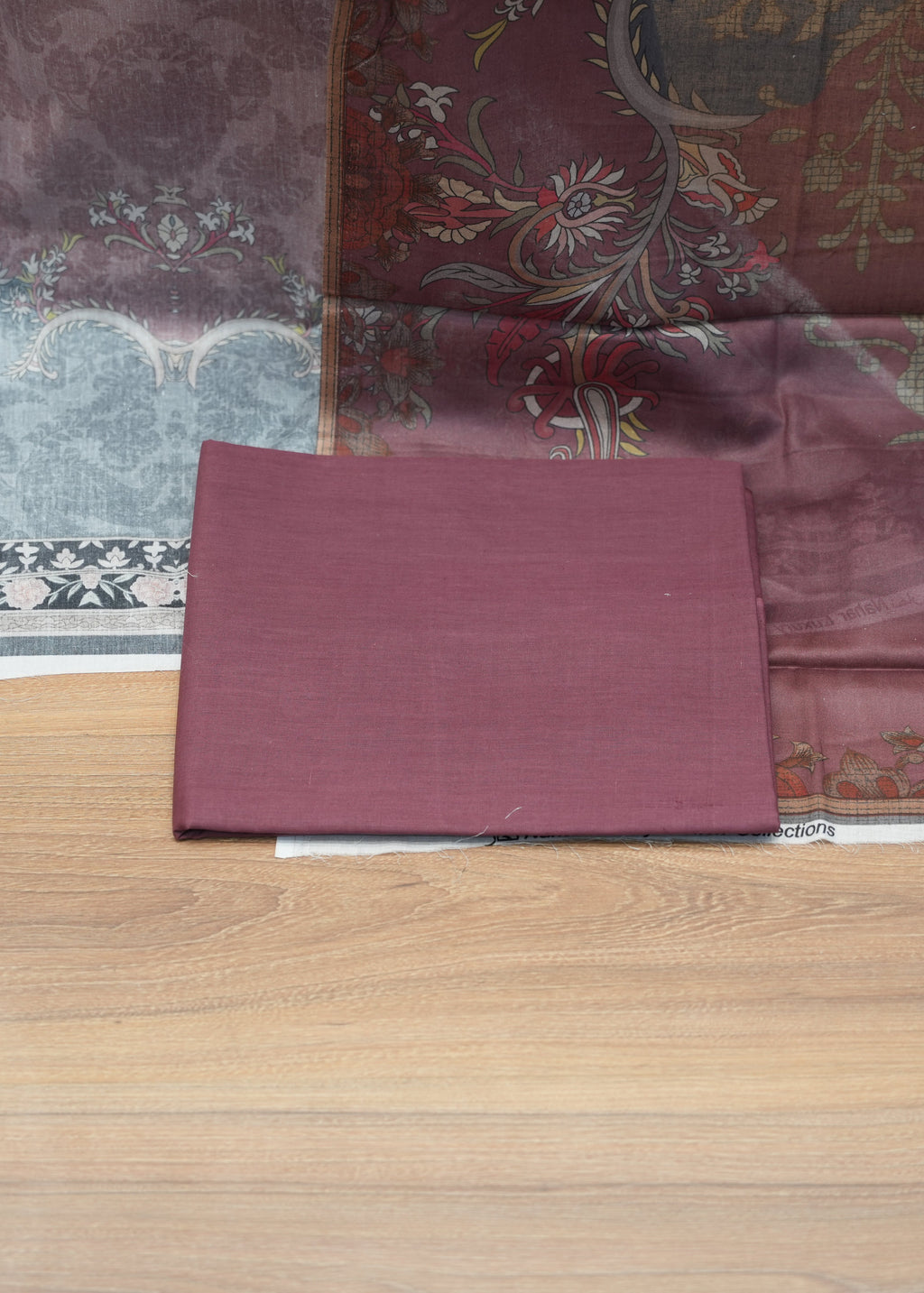 Maroon fabric swatch on a wooden surface with patterned fabric in the background