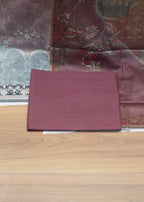 Maroon fabric swatch on a wooden surface with patterned fabric in the background