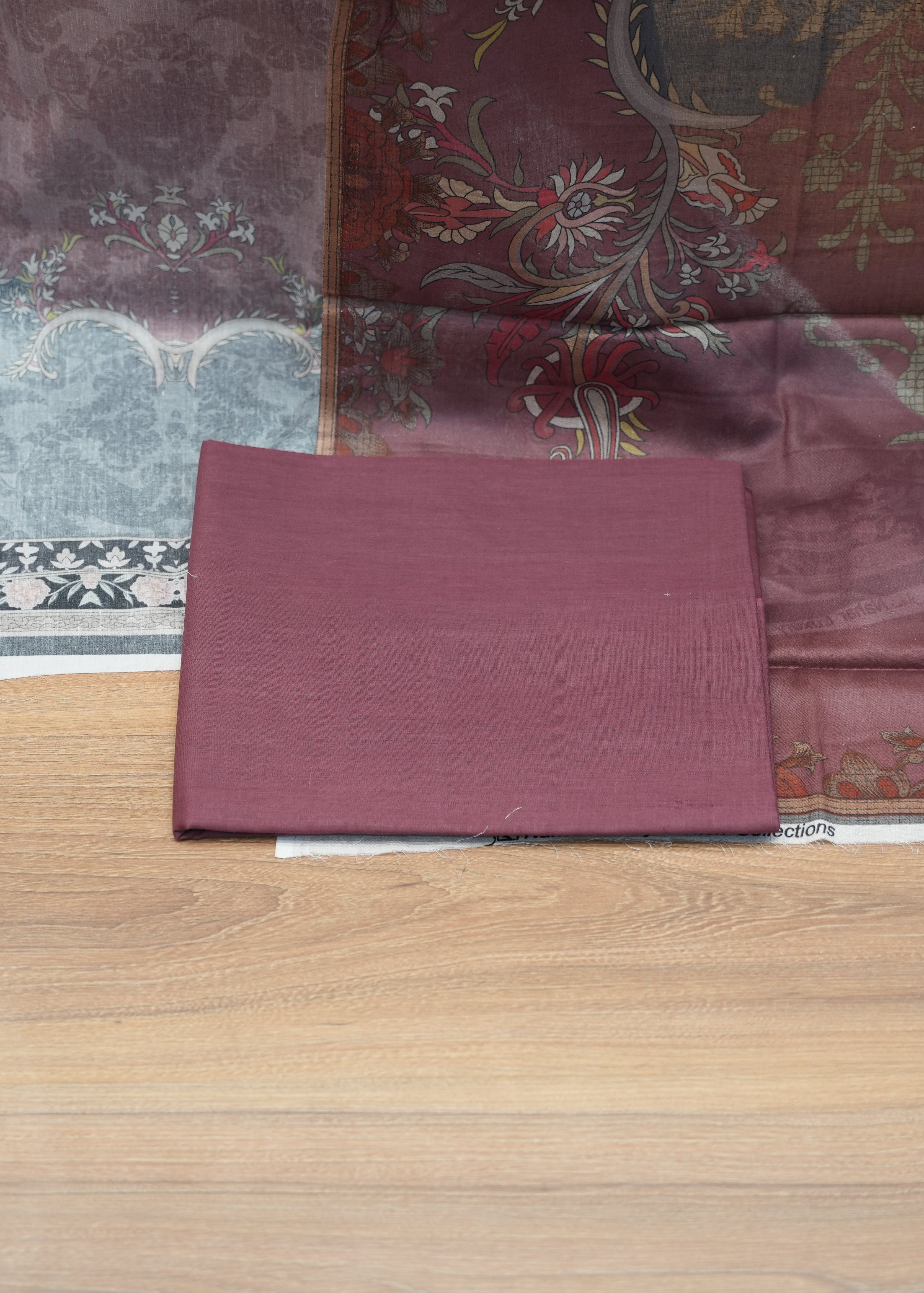 Maroon fabric swatch on a wooden surface with patterned fabric in the background
