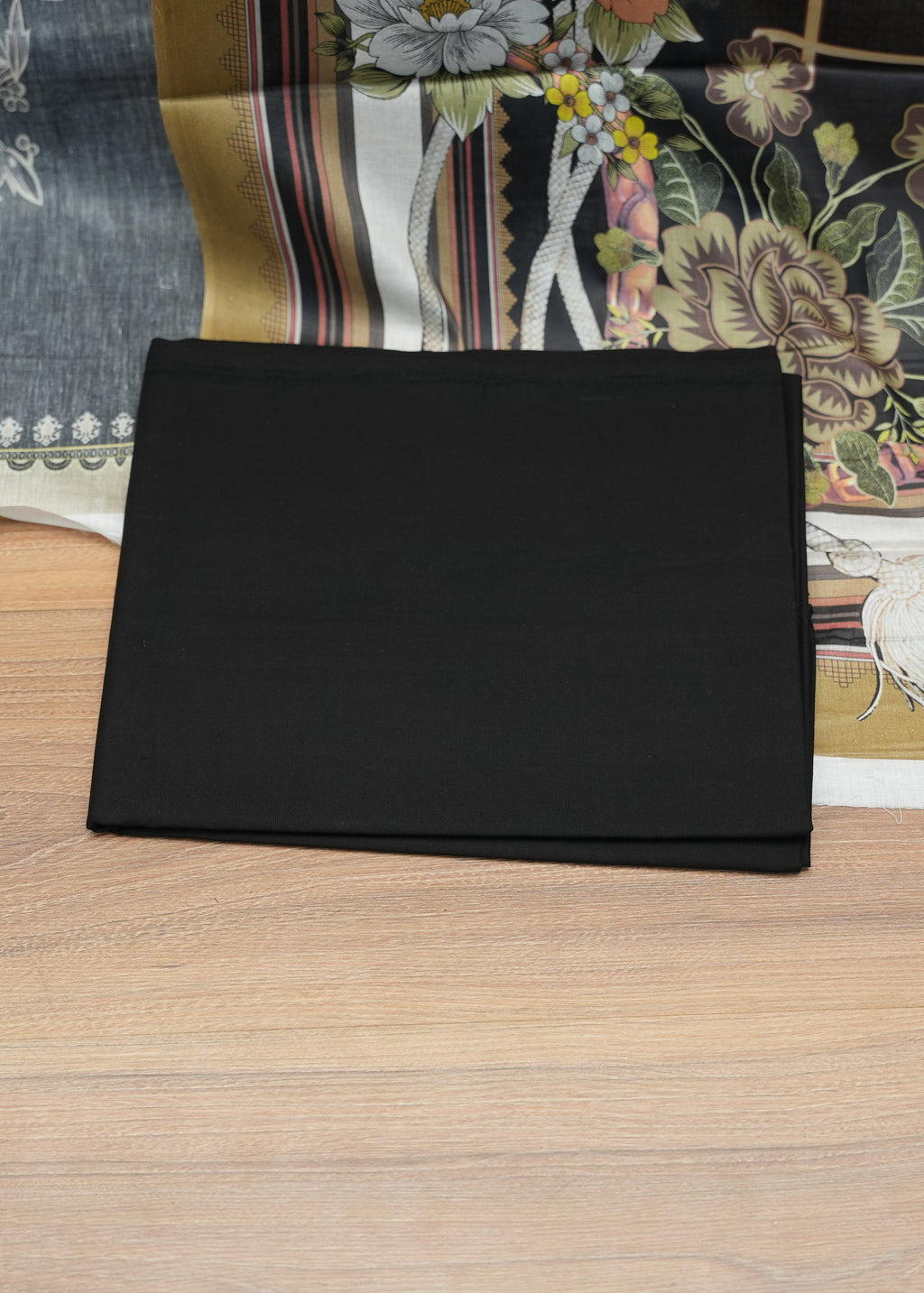 Black rectangular object on a wooden surface with a floral-patterned fabric in the background