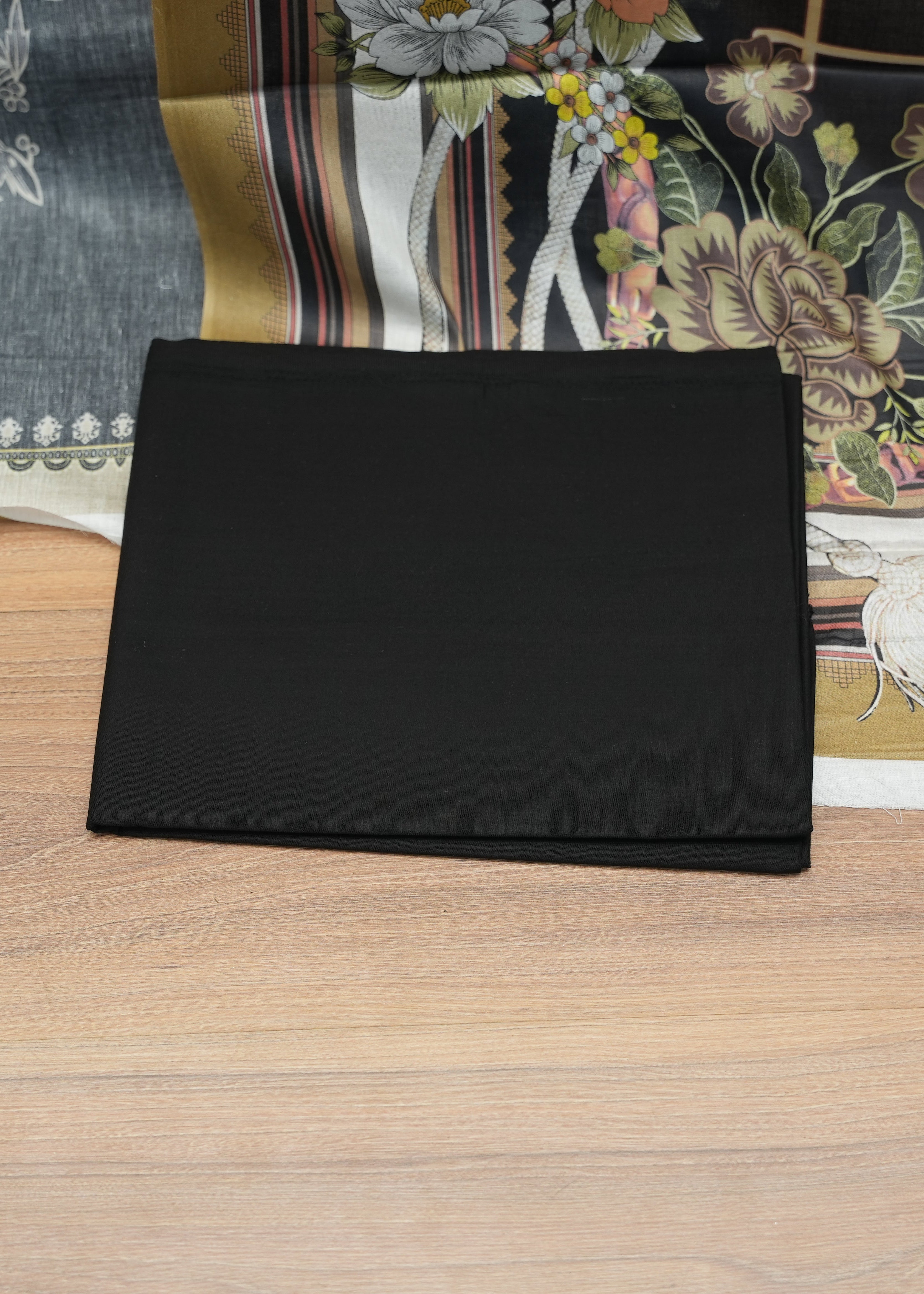 Black rectangular object on a wooden surface with a floral-patterned fabric in the background