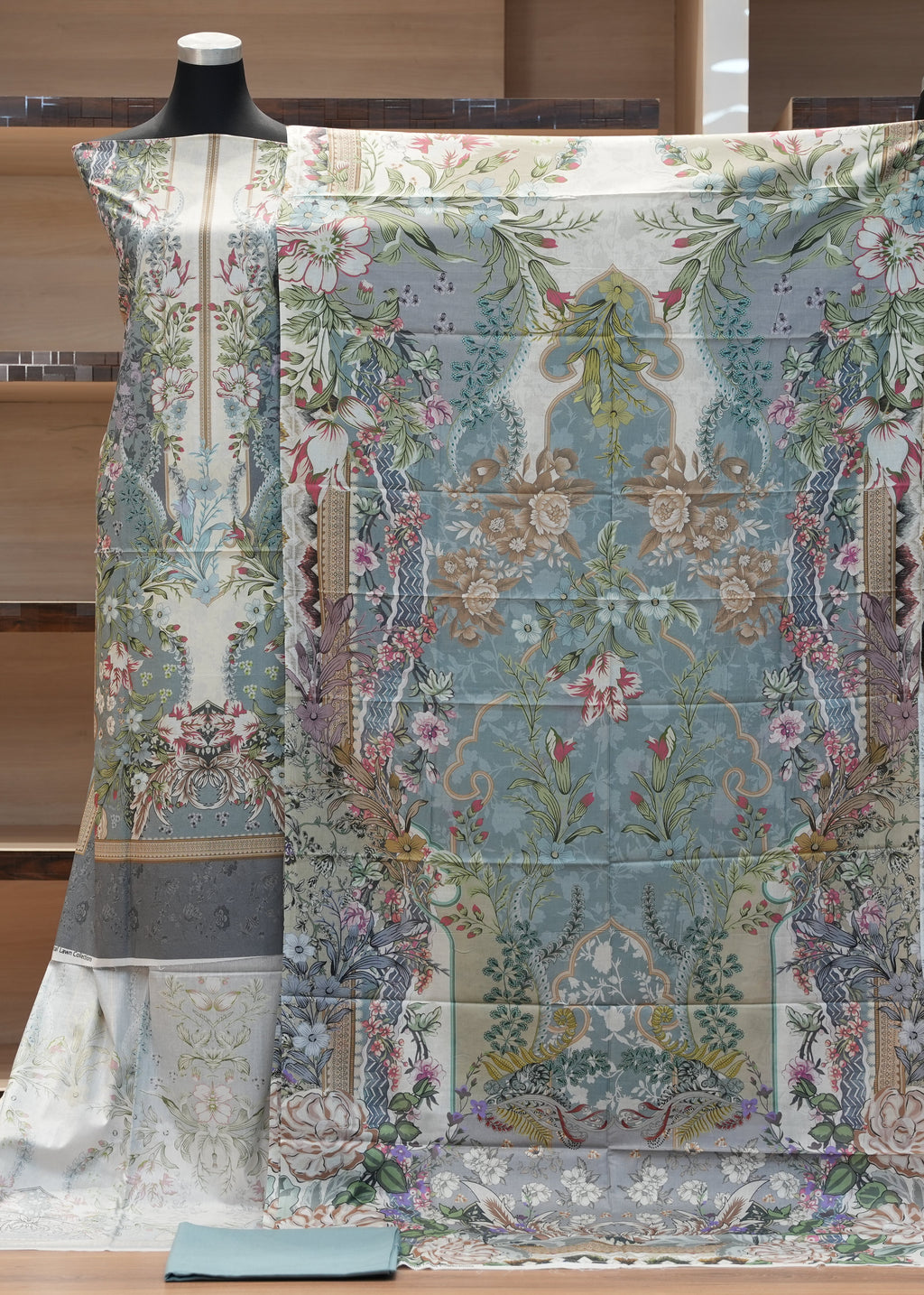 Decorative fabric with floral patterns draped over a mannequin against a wooden shelf background.
