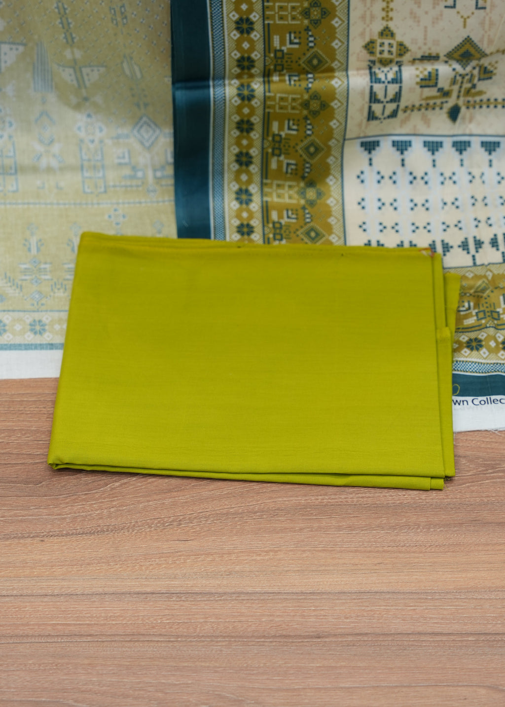 Stack of green fabric on a wooden surface with patterned fabric in the background
