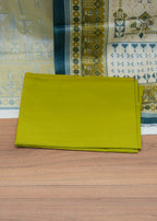Stack of green fabric on a wooden surface with patterned fabric in the background