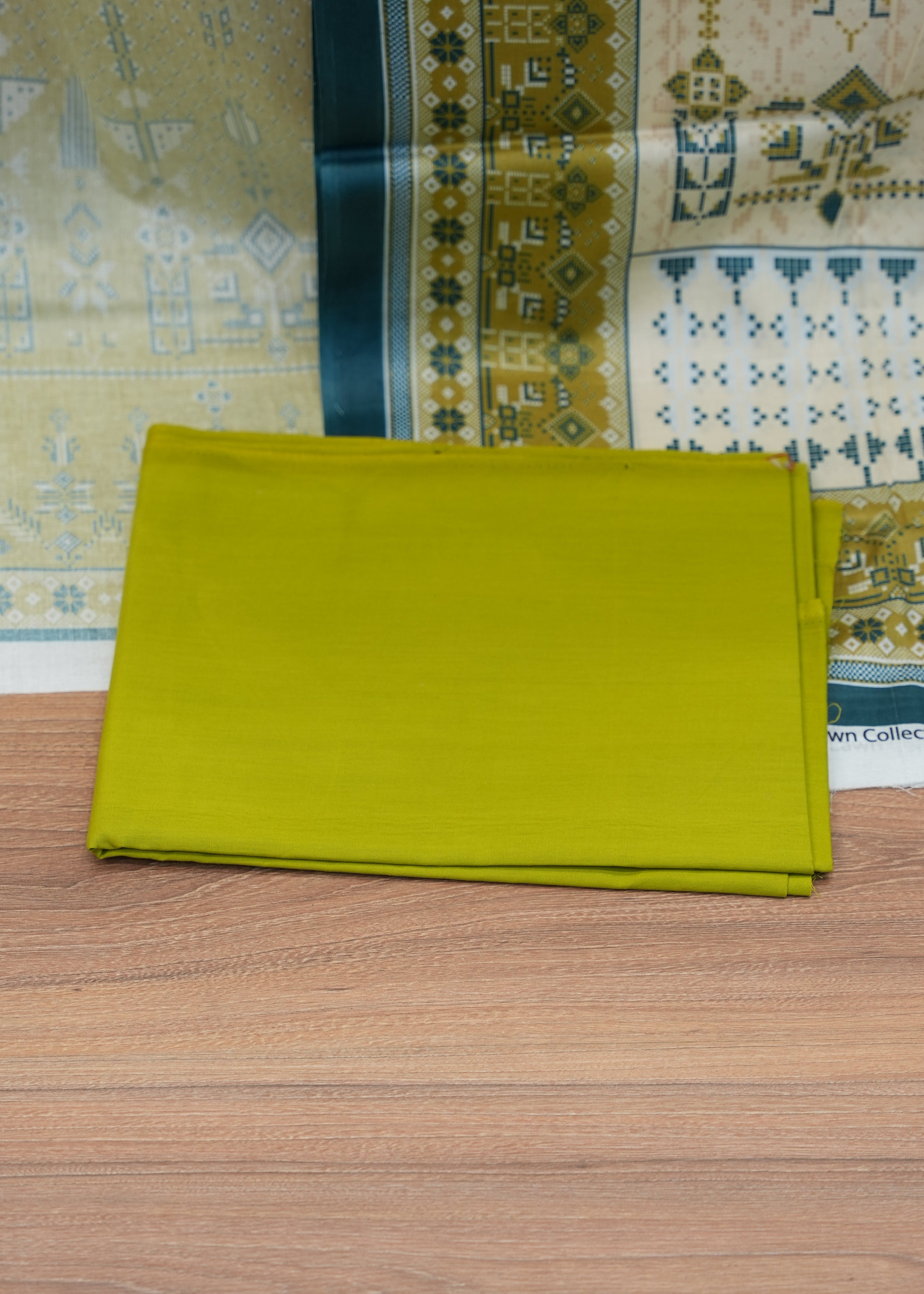 Stack of green fabric on a wooden surface with patterned fabric in the background