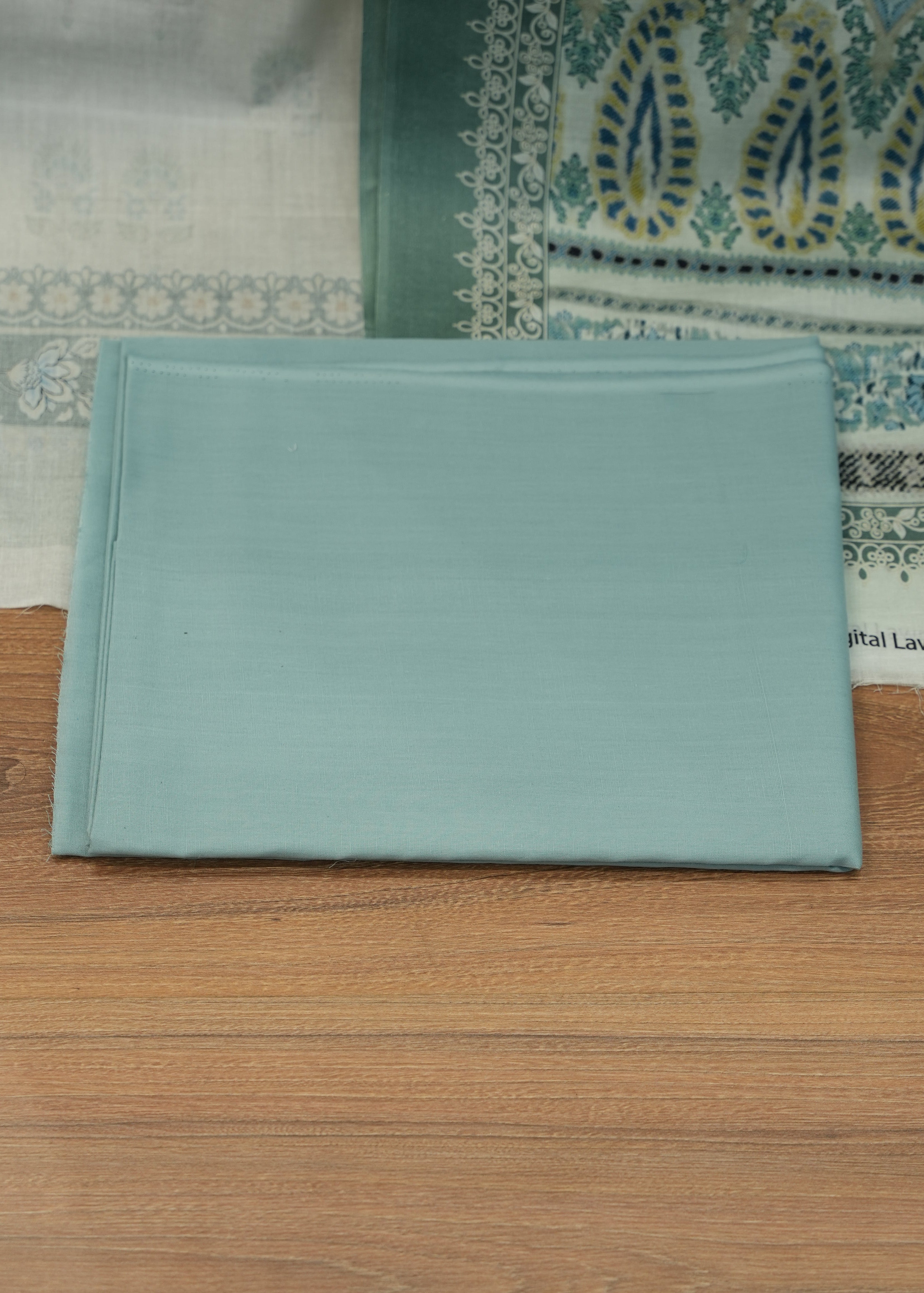 Light blue fabric sample on a wooden surface with a patterned rug underneath