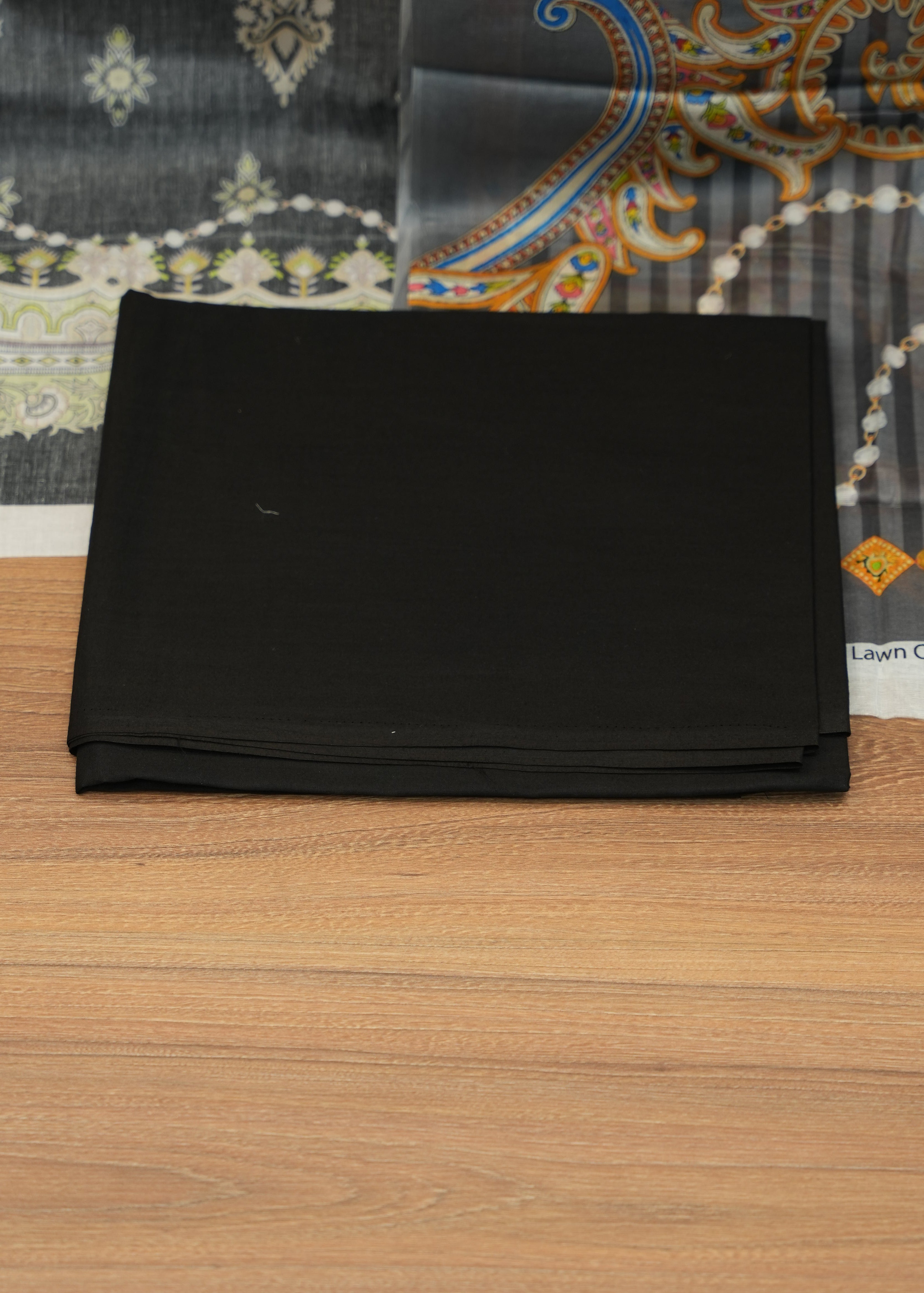 Black book on a wooden surface with a patterned fabric background