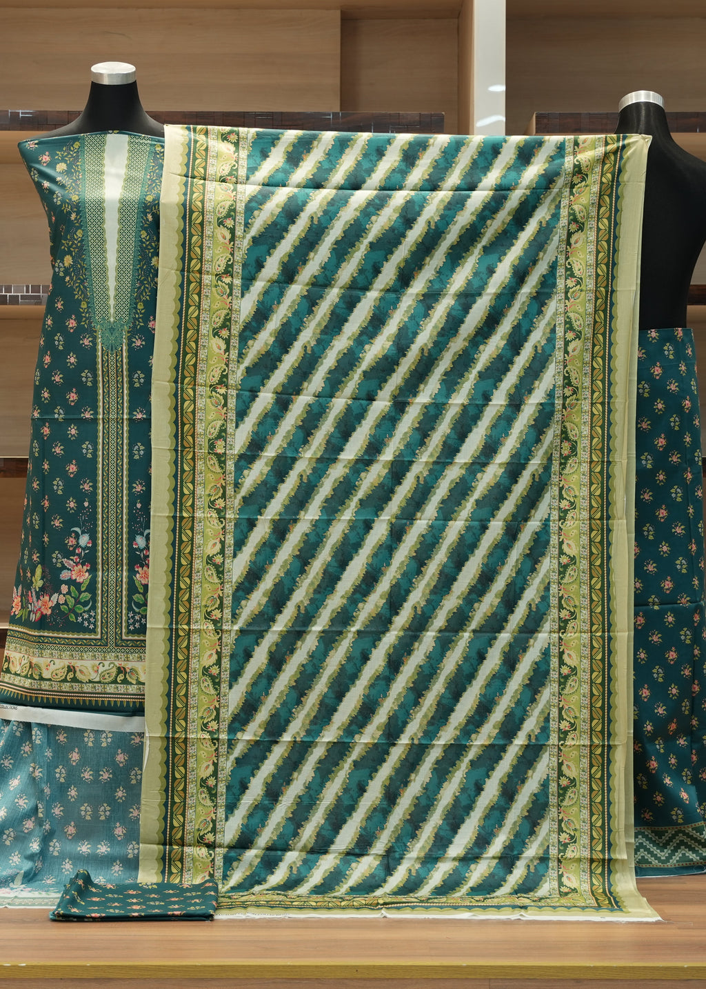 Traditional green and blue patterned fabric on a mannequin against a wooden shelf background