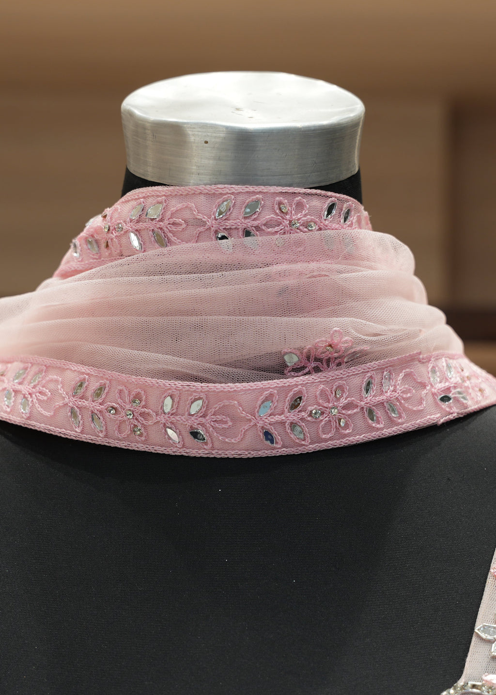 Mannequin wearing a pink embroidered top and matching scarf with a blurred background