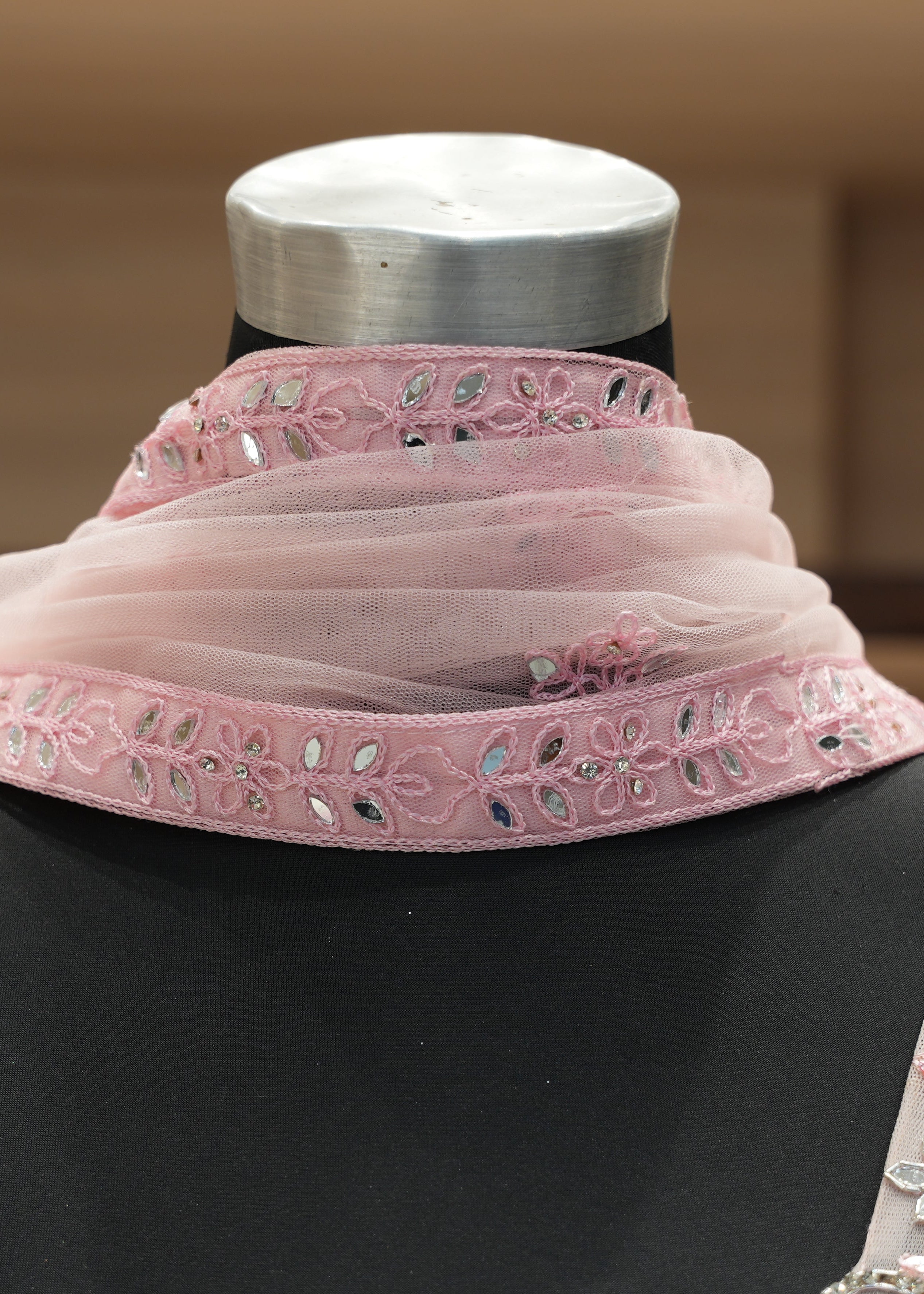 Mannequin wearing a pink embroidered top and matching scarf with a blurred background
