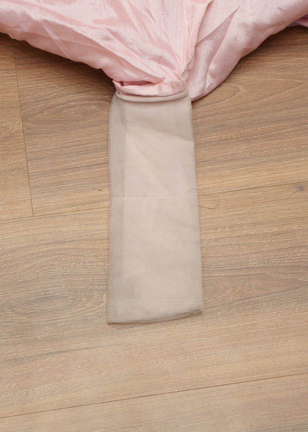 Close-up of a pink fabric with a beige trim on a wooden floor.