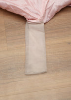 Close-up of a pink fabric with a beige trim on a wooden floor.