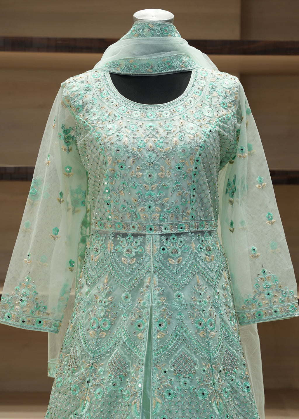 Teal embroidered garment on a mannequin against a neutral background