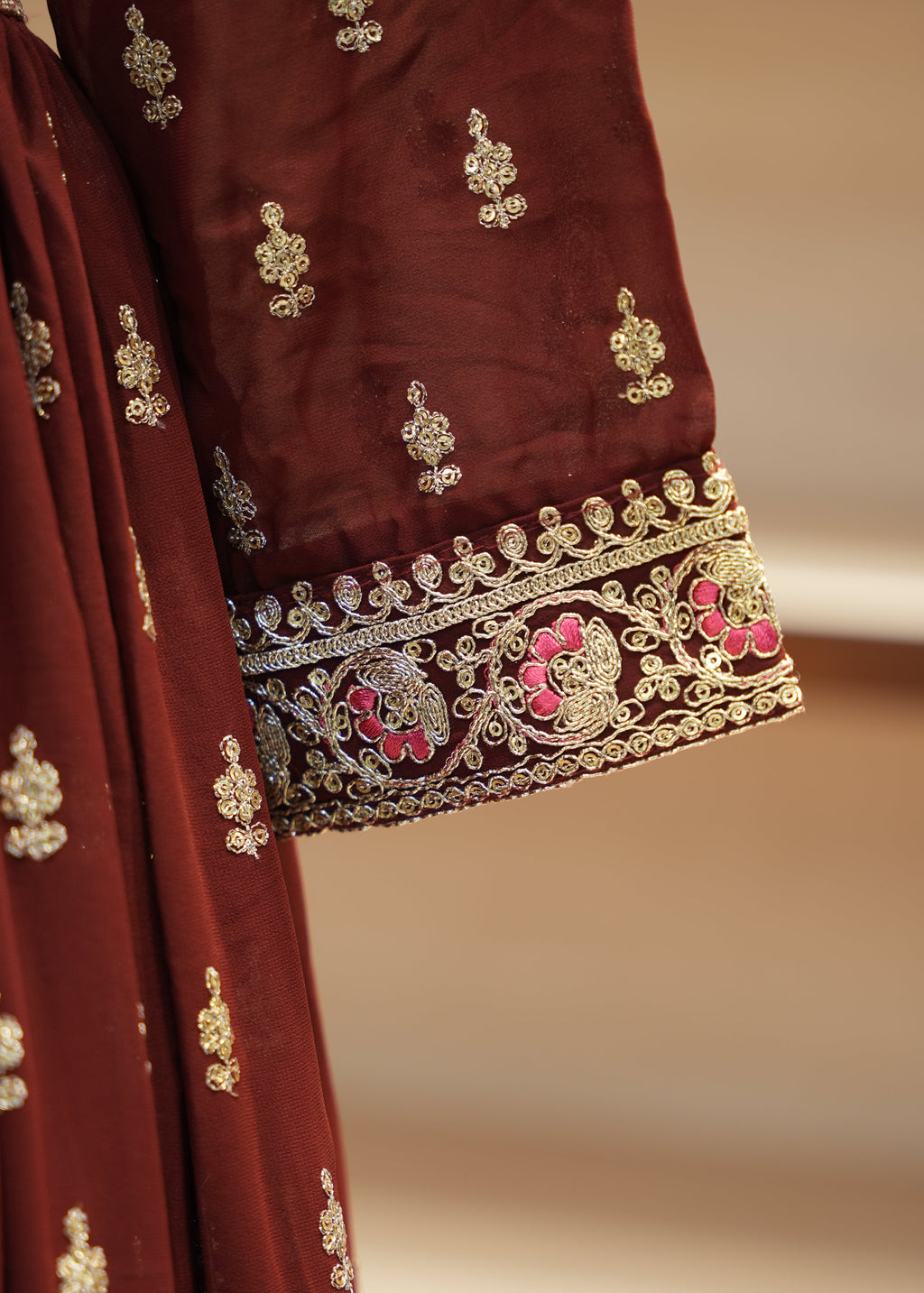 Maroon fabric with gold and pink embroidery on a neutral background