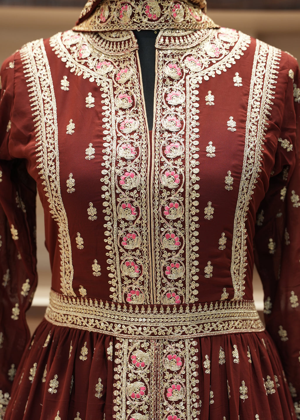 Close-up of a maroon fabric with intricate gold and pink embroidery.