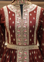 Close-up of a maroon fabric with intricate gold and pink embroidery.