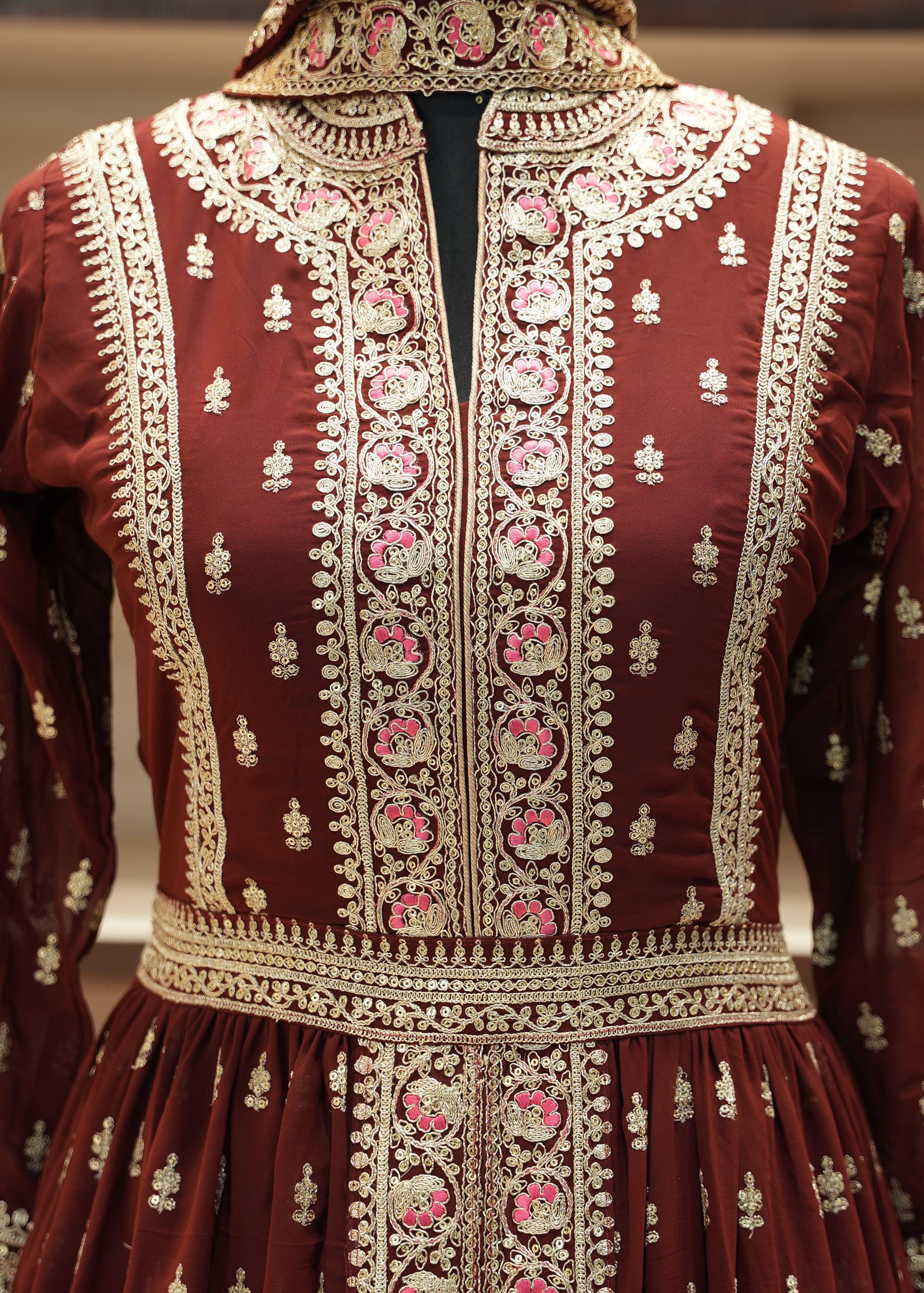 Close-up of a maroon fabric with intricate gold and pink embroidery.