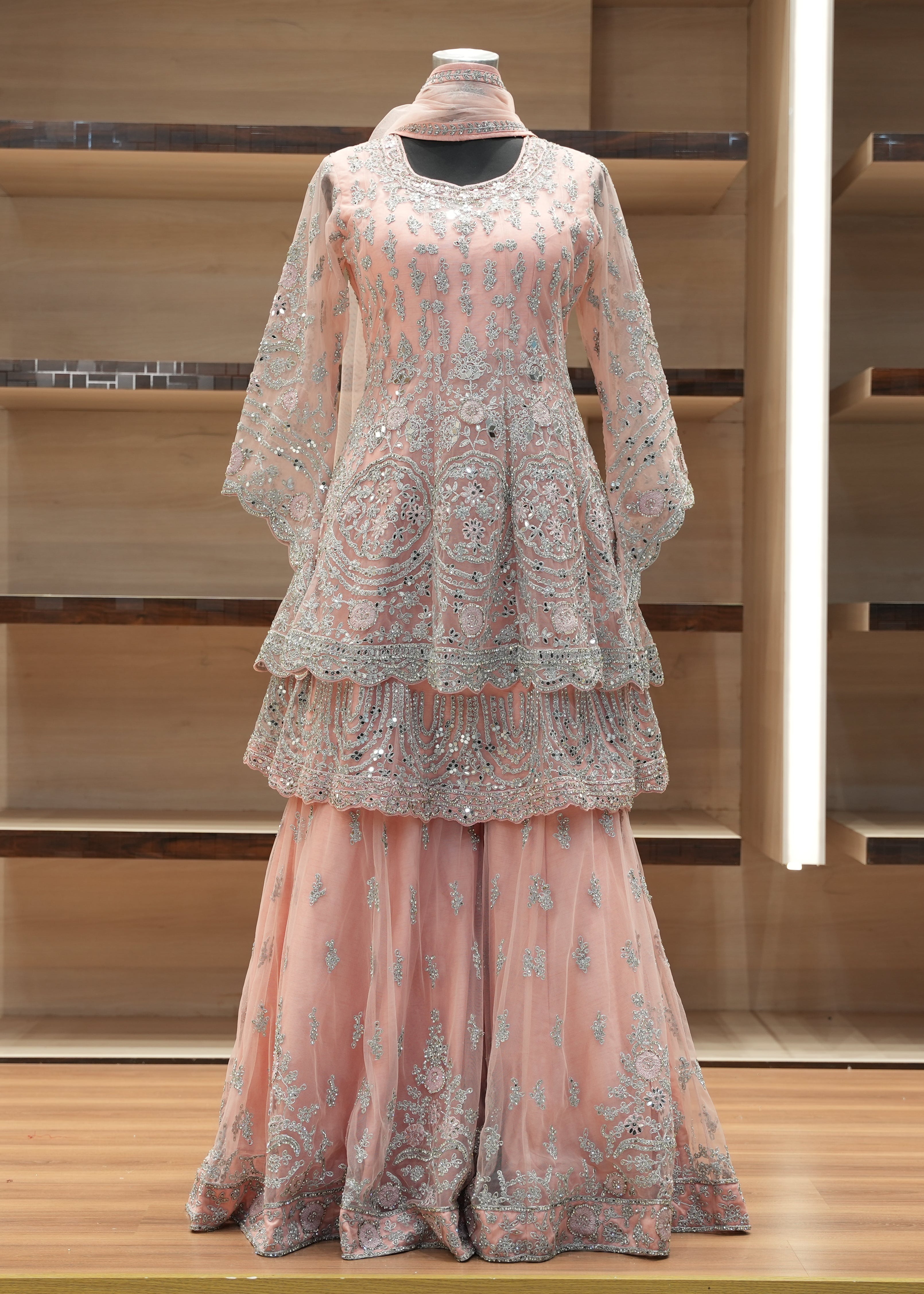 Pink embroidered outfit on a mannequin against a wooden shelf background